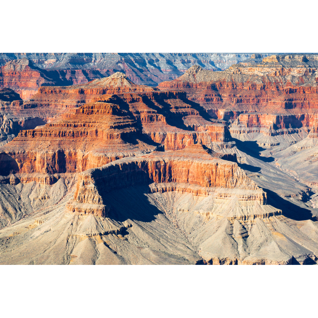 Panoramic view of layered sandstone mesas and buttes in the Grand Canyon under warm desert light.