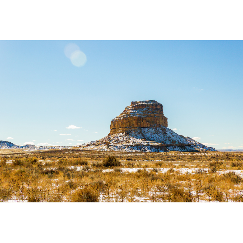 Solitary desert butte with light snow covering set against an expansive Southwest landscape.