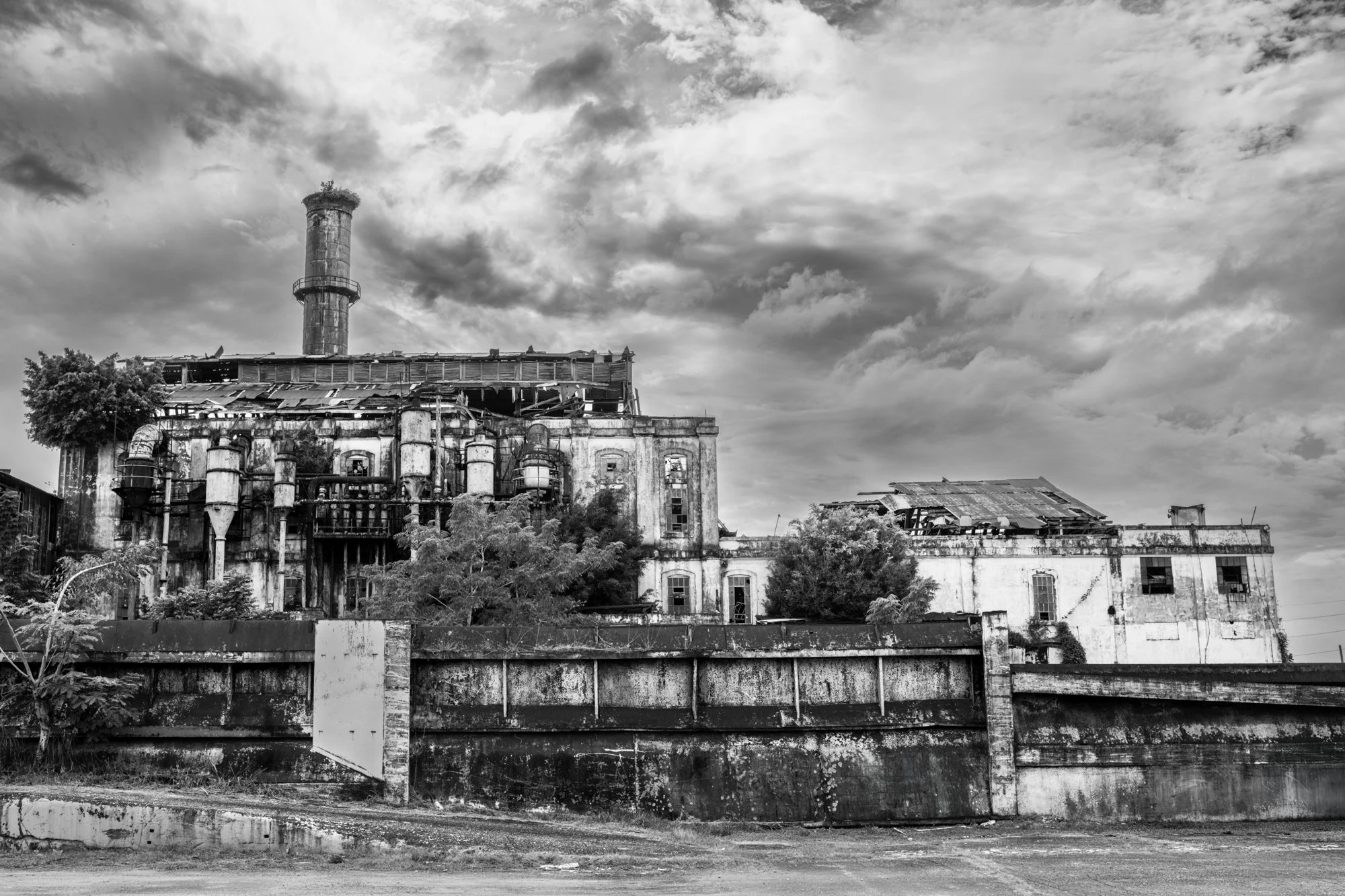 Black-and-white fine art print of Central Coloso beneath dramatic clouds in Aguada, Puerto Rico. Historic industrial wall art with a quiet, atmospheric presence.