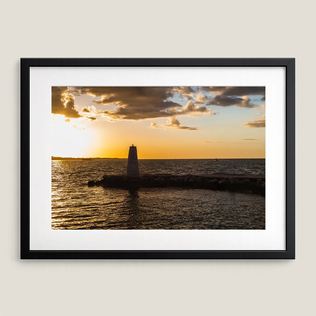 Golden hour harbor beacon photograph in black frame with white mat.