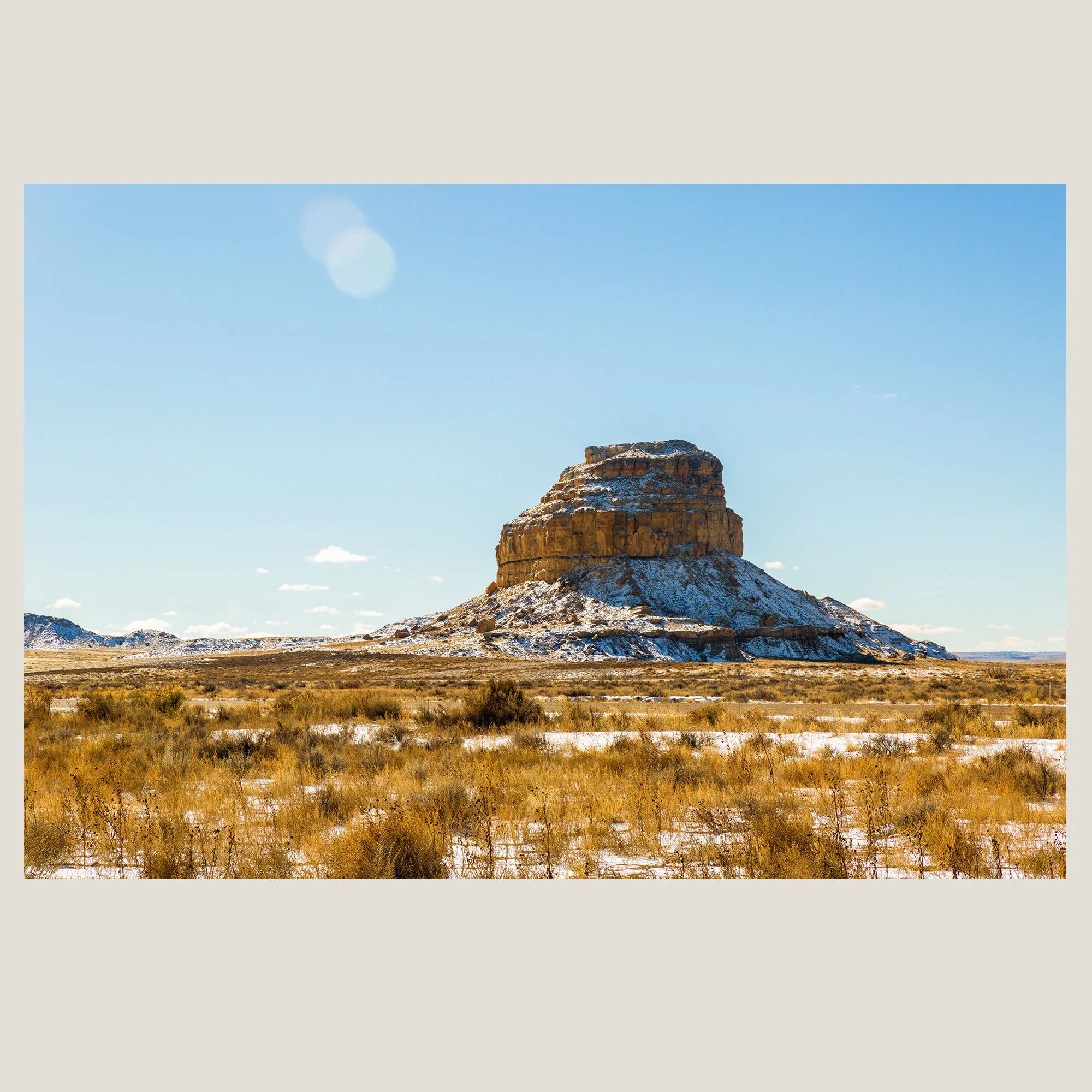 Isolated desert butte dusted with snow rising above a wide Southwest desert landscape.