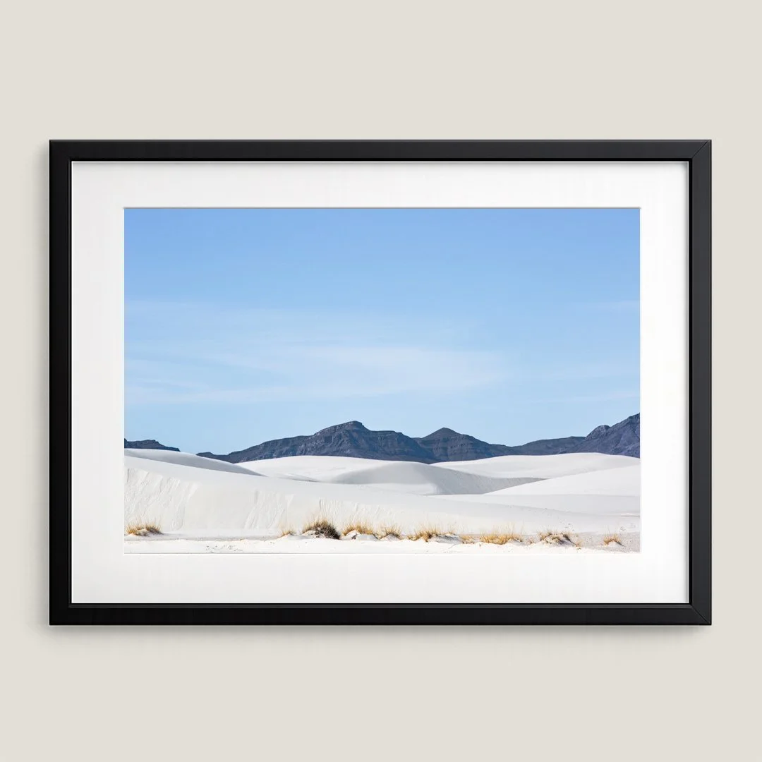 Framed White Sands landscape print with black frame and white mat, featuring rolling gypsum dunes and distant mountains.