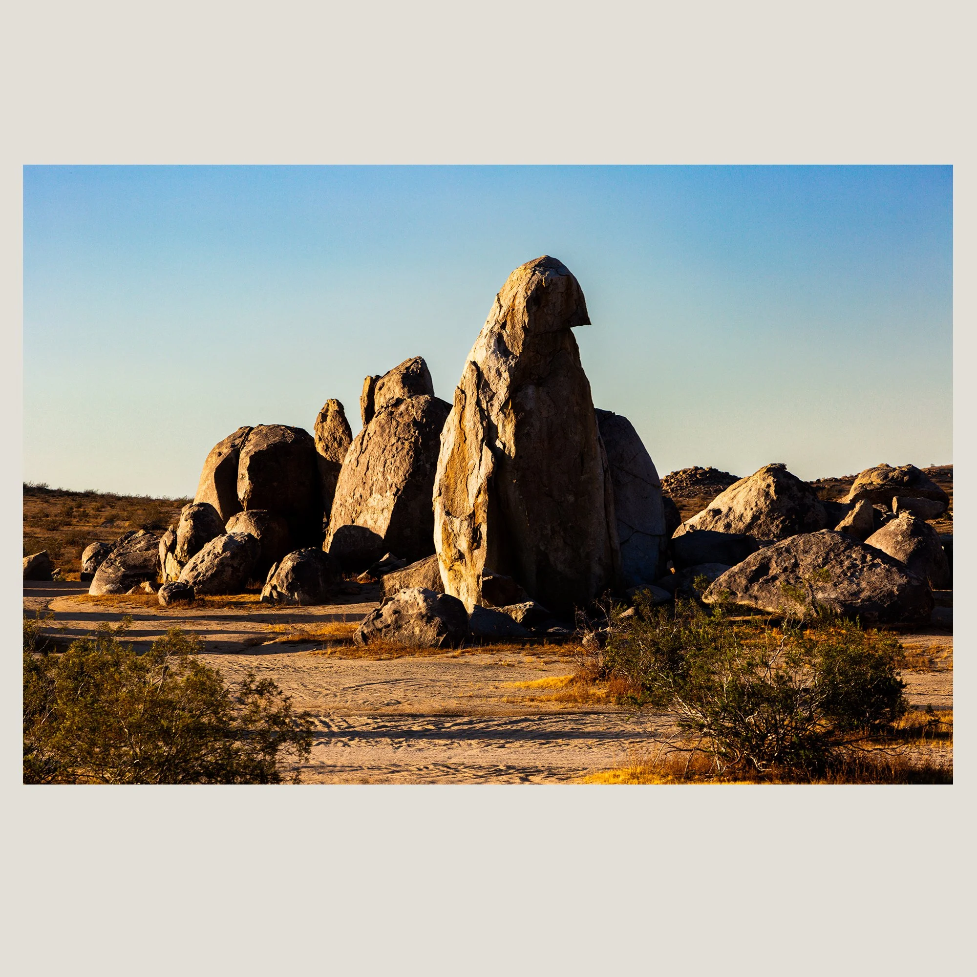 Warm evening light illuminating sculpted boulder formations in a rugged Southwest desert landscape.