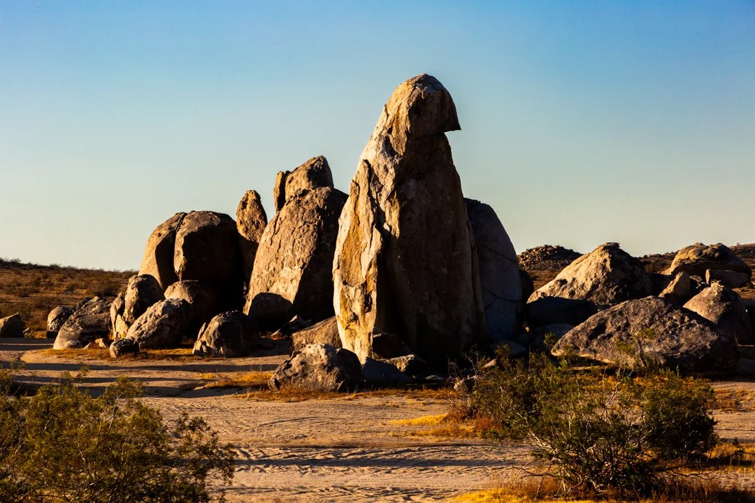 Golden evening light illuminating weathered desert boulders in the Mojave Desert near Trona, California, revealing rich textures, warm earth tones, and sculptural rock formations beneath a clear sky.