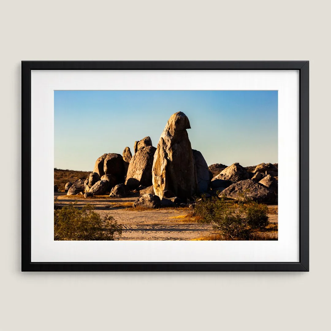 Framed Southwest desert landscape print with black frame and white mat, featuring sculpted boulder formations at sunset.