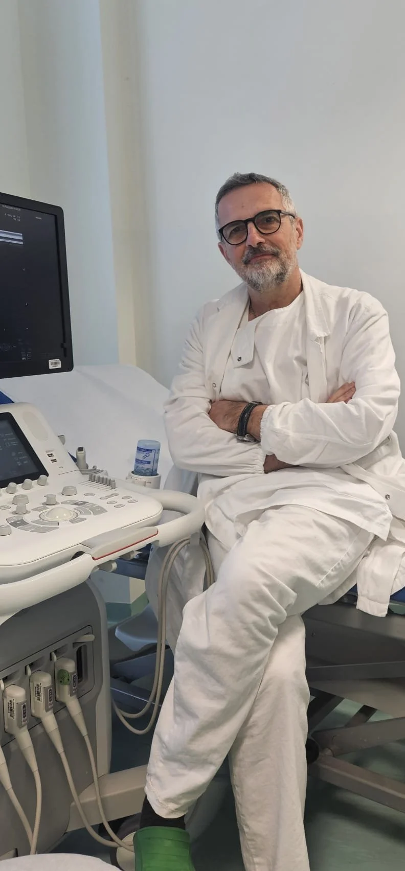 Uomo medico in divisa bianca seduto accanto a un lettino d'ospedale, con apparecchiature mediche e monitor in ospedale