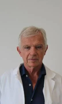 Uomo anziano con capelli bianchi, in camice bianco, sfondo bianco.