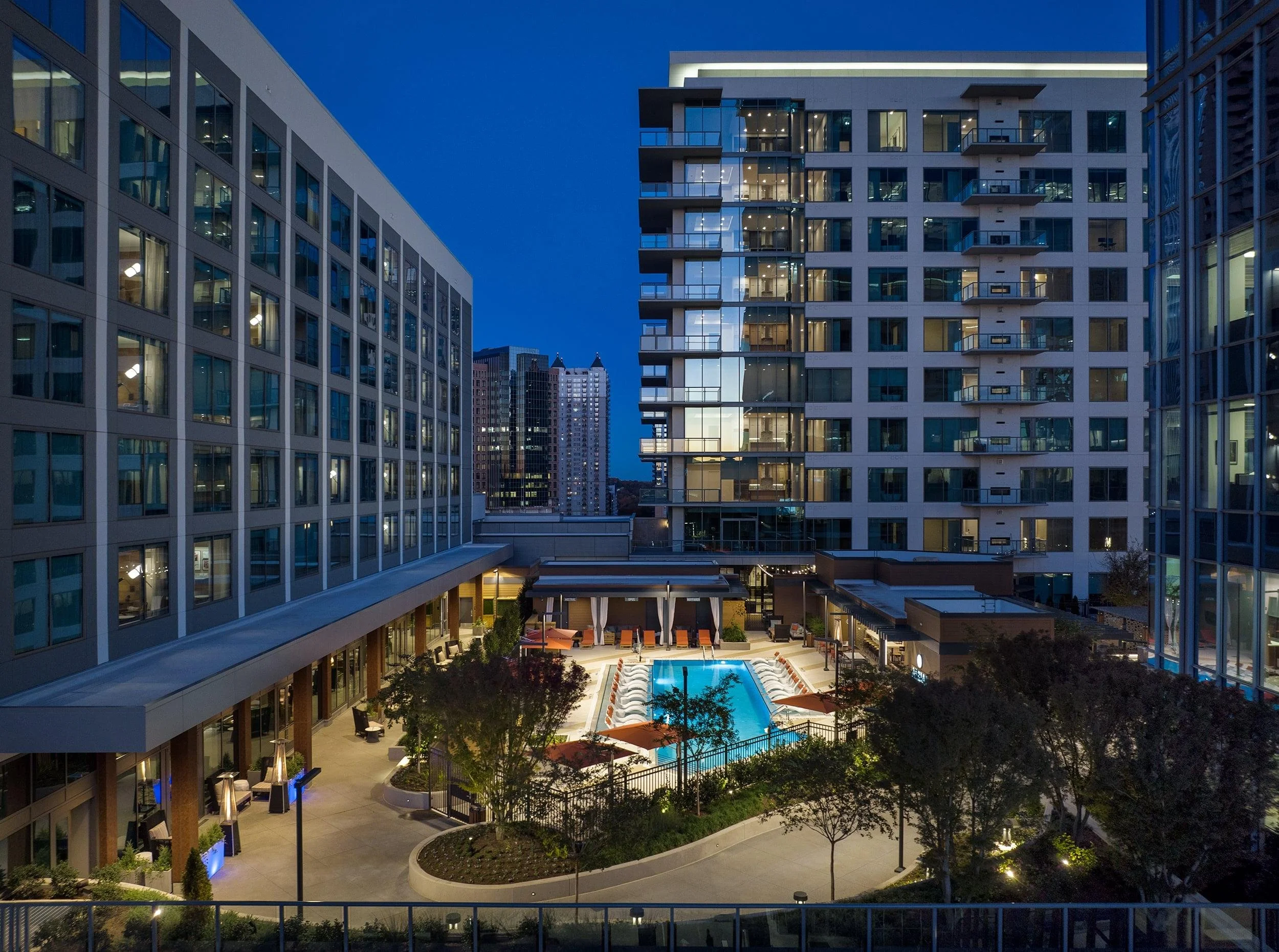 Nighttime view of Epicurean Atlanta, Autograph Collection hotel with lit windows, a swimming pool, and outdoor seating area in a city.
