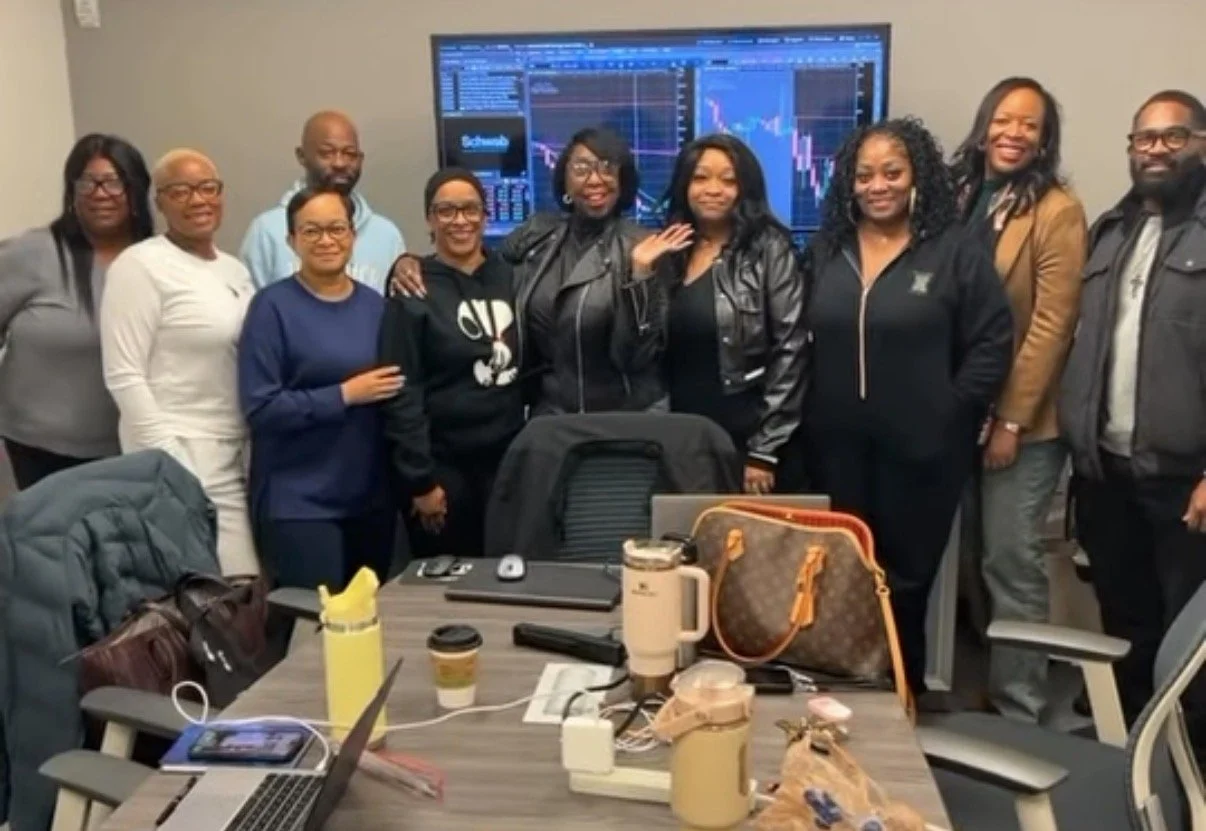 Group of eleven diverse people from the Dripper Community standing in a conference room, smiling, with a large screen displaying stock market charts in the background.