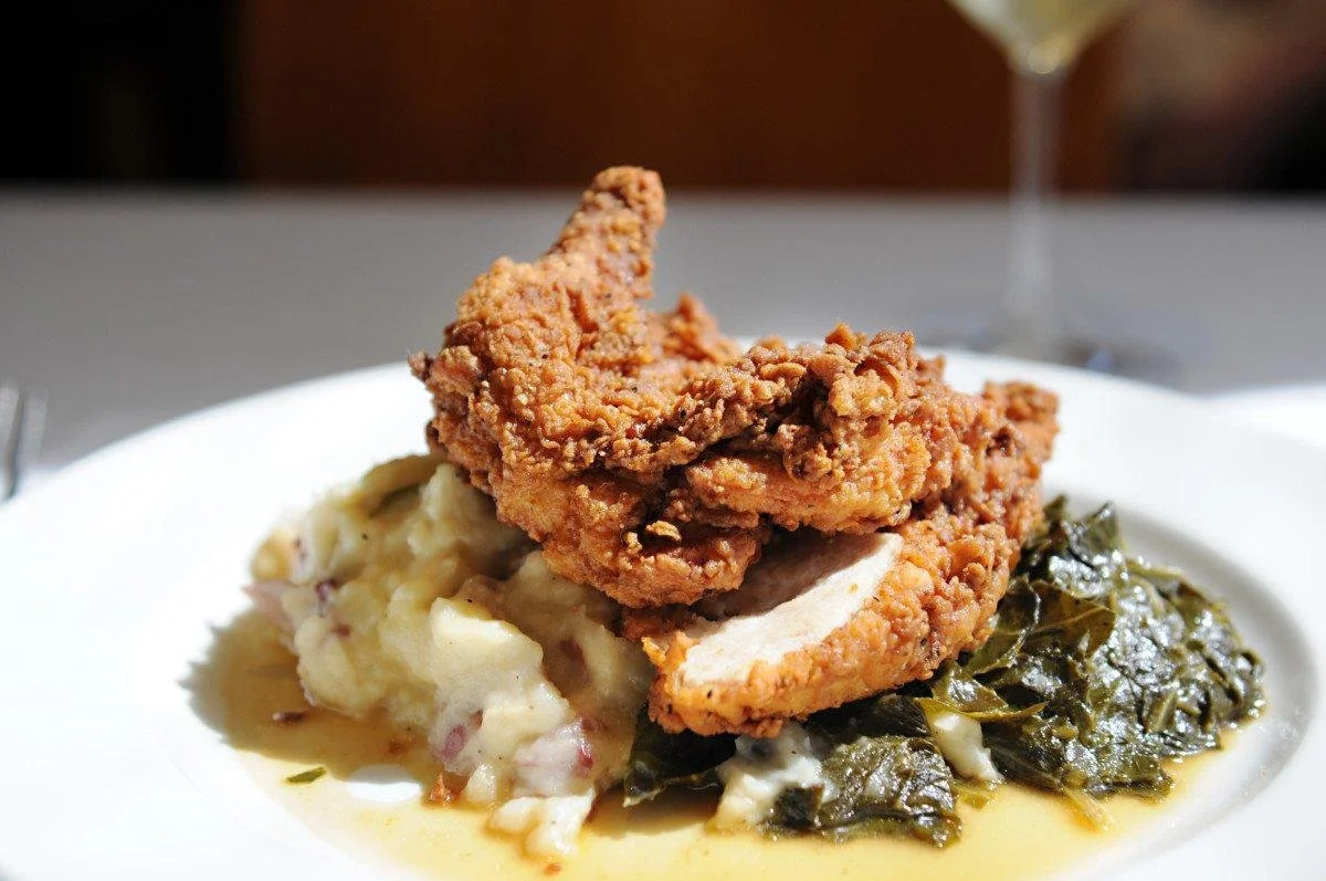 Fried chicken from South City Kitchen on top of mashed potatoes and cooked collard greens on a white plate with white tablecloths.