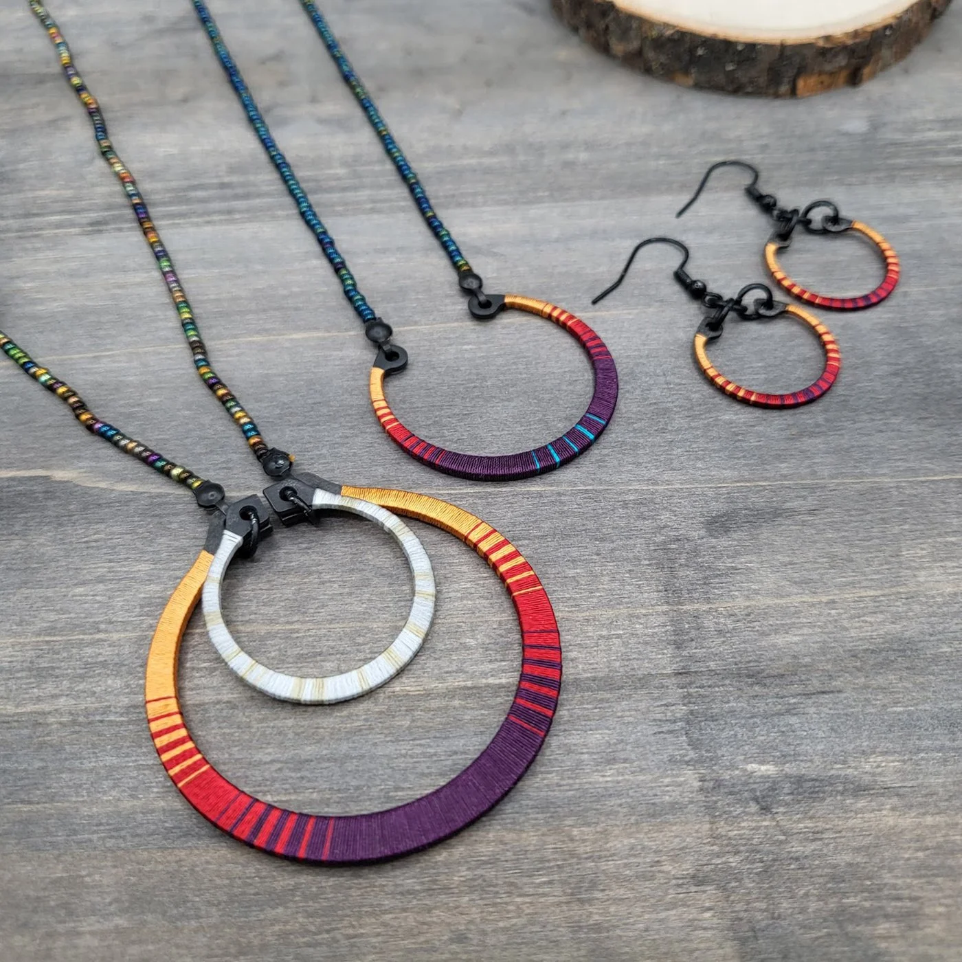 Colorful jewelry set including bracelets and earrings with circular designs, decorated with multicolored thread and beads, displayed on a wooden surface.