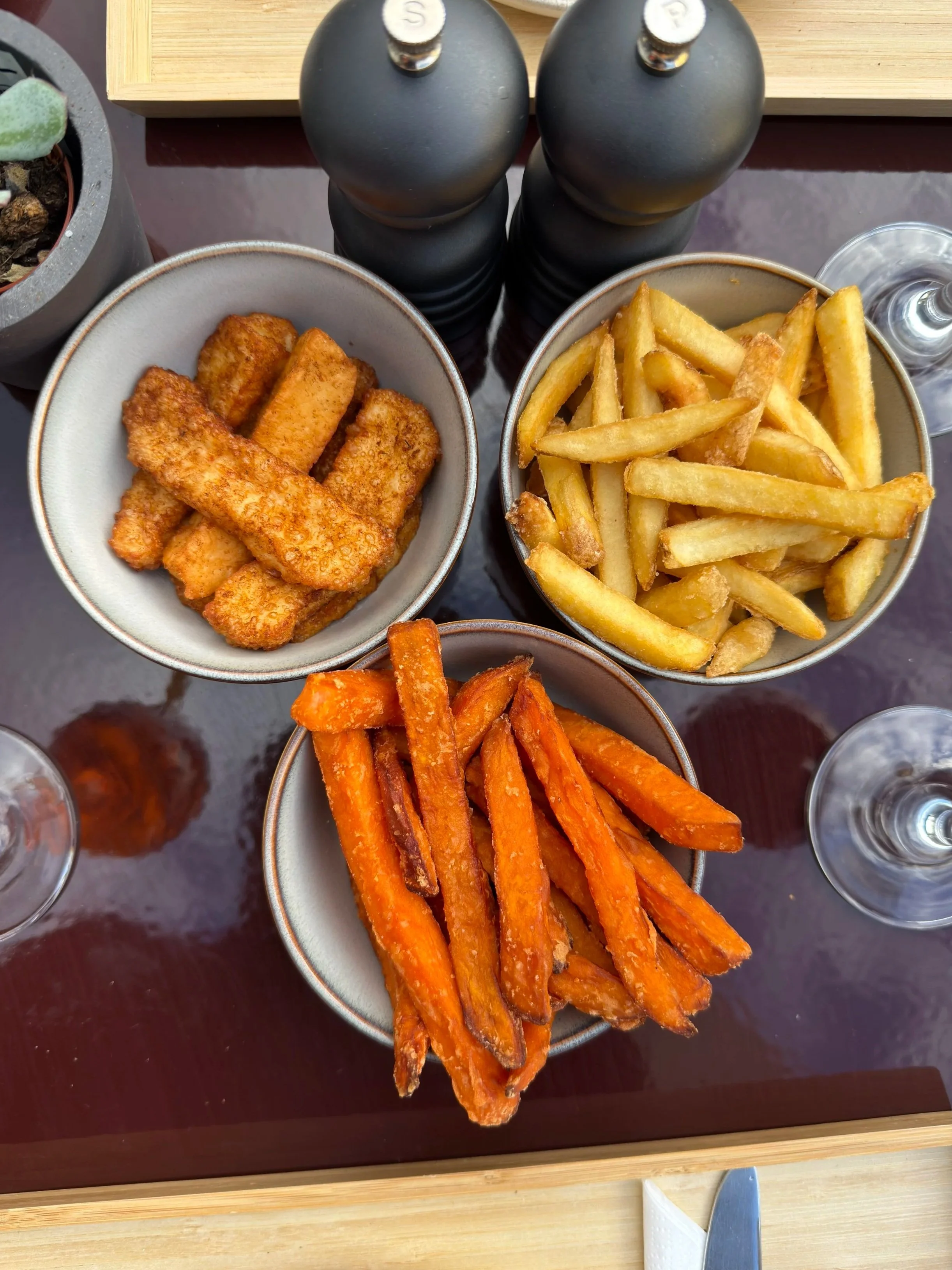 Three bowls of French fries and sweet potato fries on a table with salt and pepper shakers and water glasses.