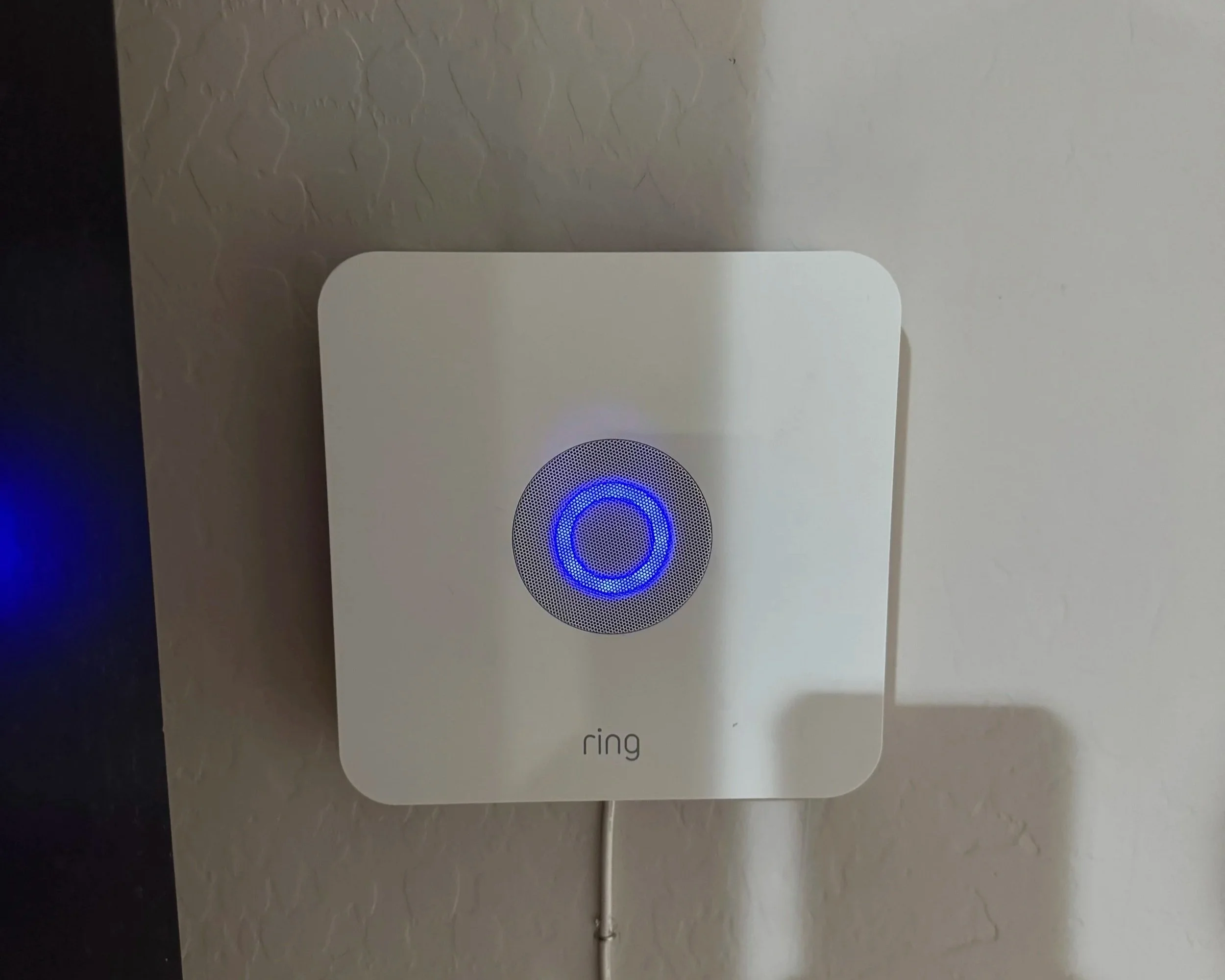 A white Ring doorbell on a wall with a blue illuminated circle in the center.
