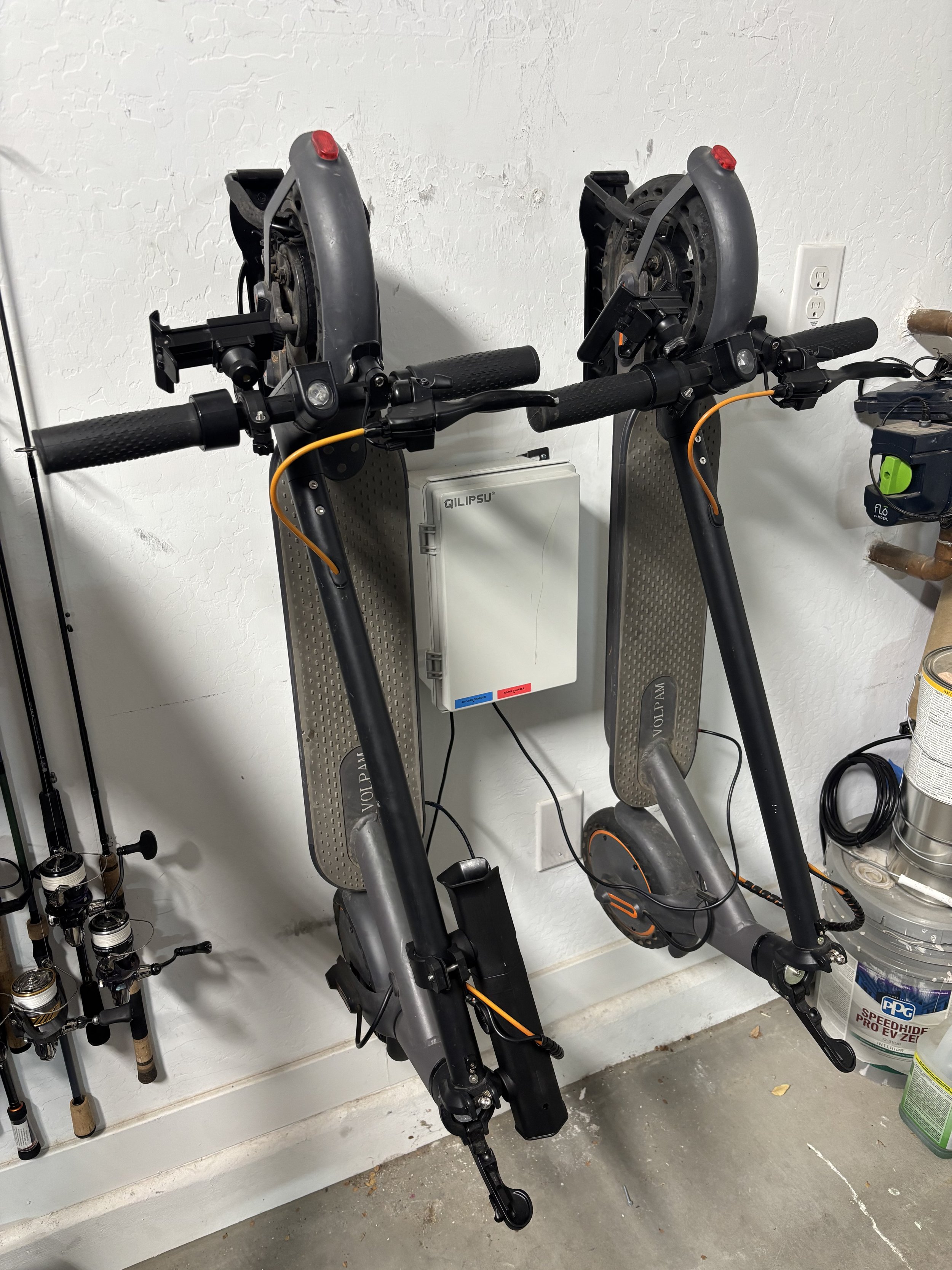Two electric bicycles hanging on a white textured wall in a garage or storage area.