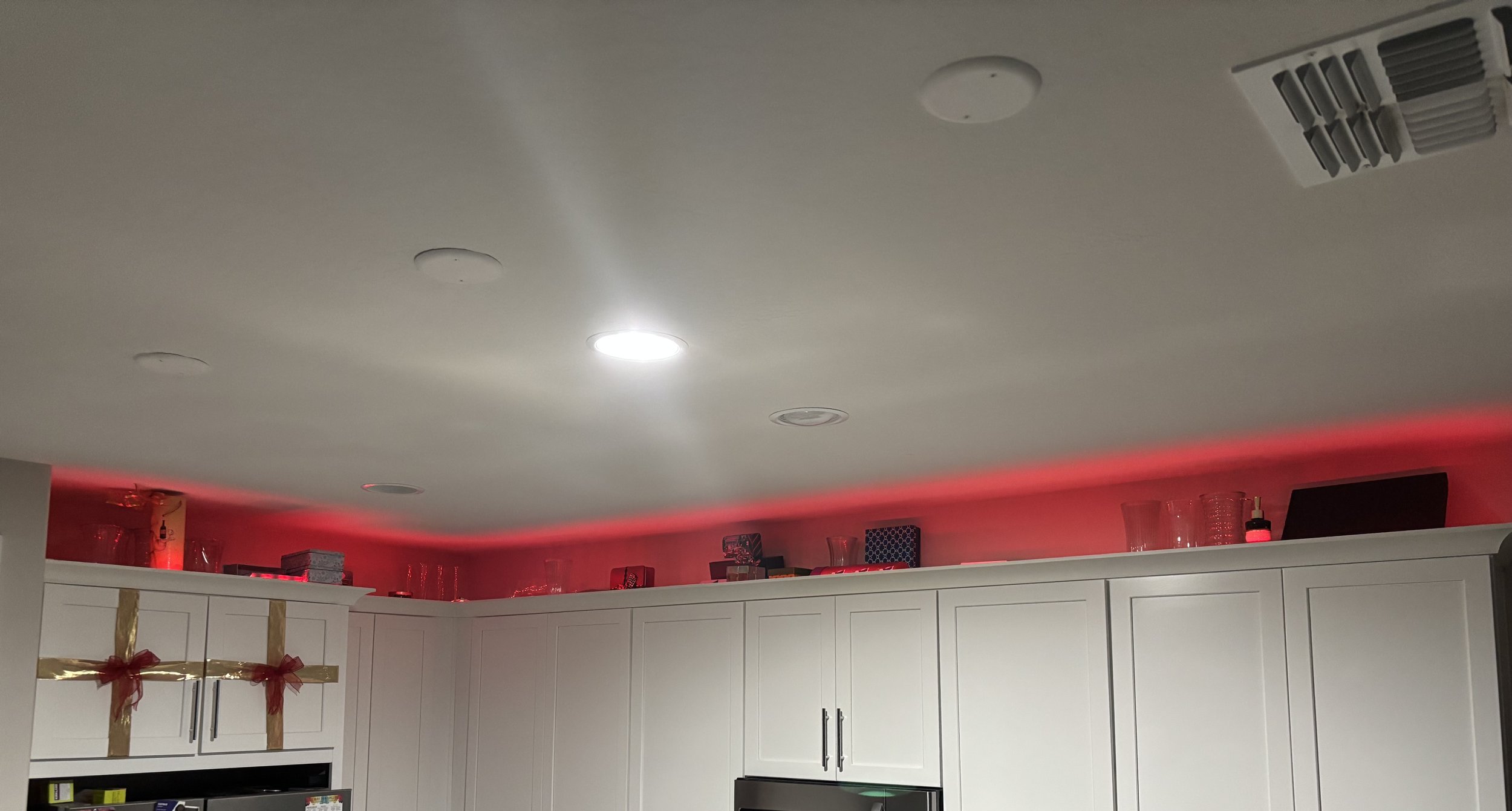 Kitchen with white cabinets and a red LED strip light above the cabinets, with various glasses and containers on top.