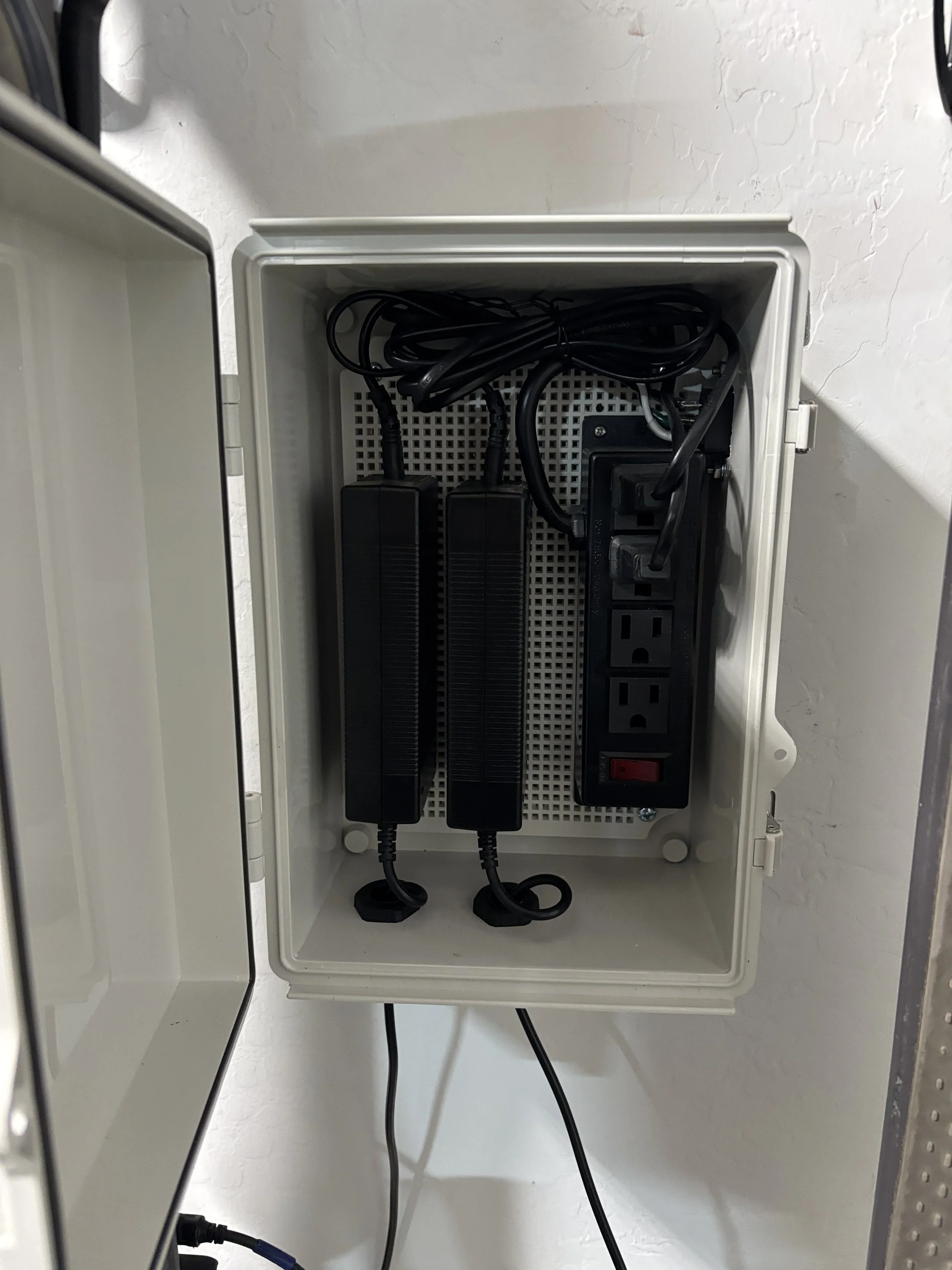 Electrical box with two black surge protectors, power strip, and multiple cords inside.