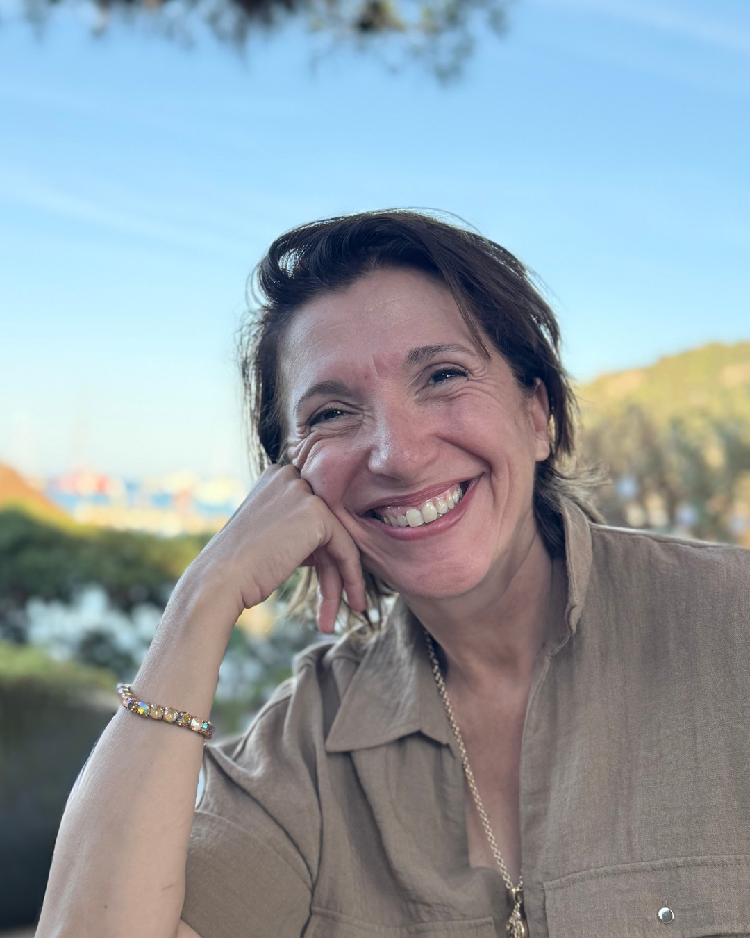 Portrait of Nathalie Colin smiling outdoors on a sunny day, with trees and buildings in the background.