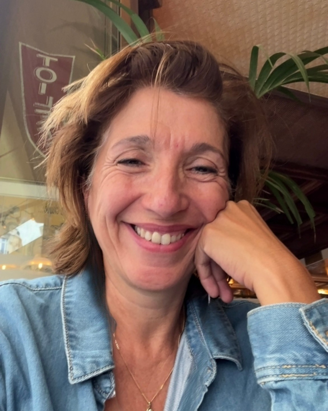 Portrait of Nathalie Colin smiling in a café setting, with plants and warm light in the background.