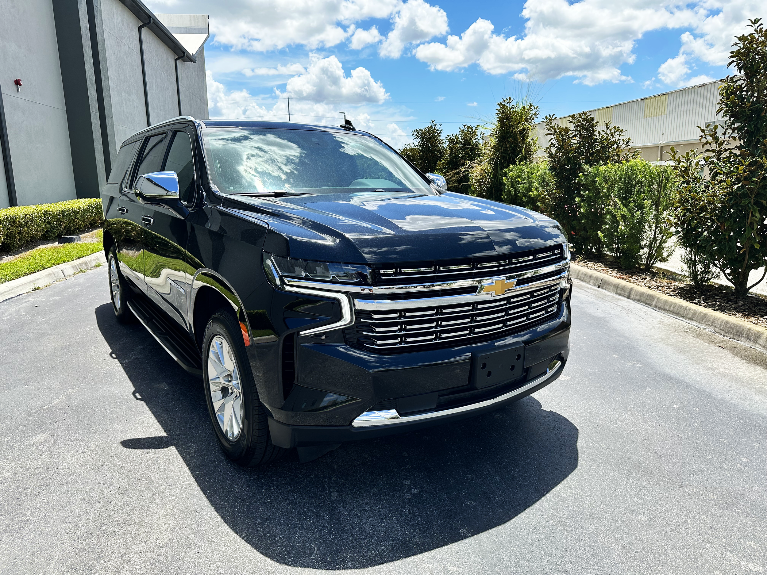 Black Chevrolet SUV parked on a sunny day near a building and shrubs.