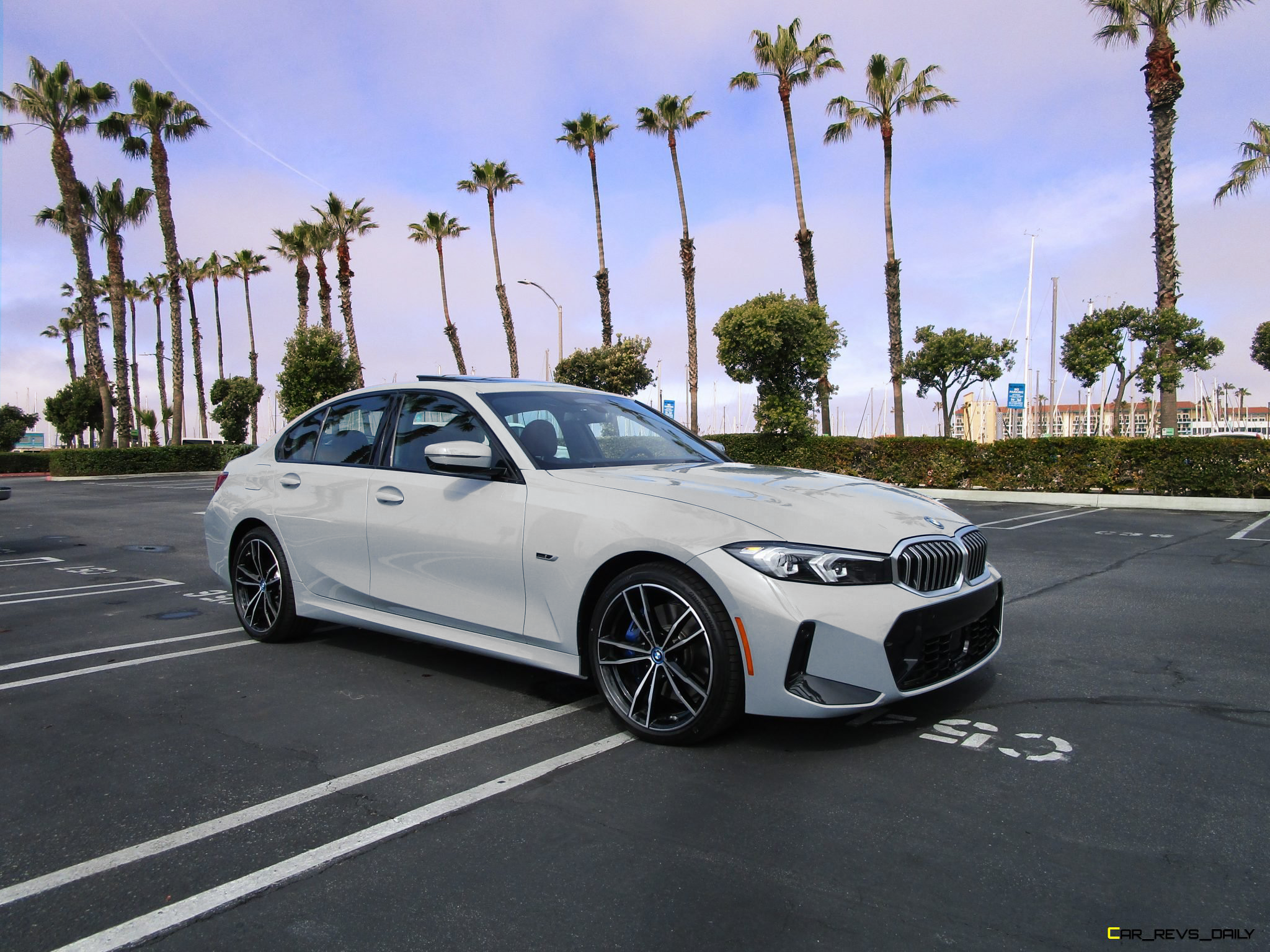 White BMW sedan parked in outdoor lot with palm trees in the background.