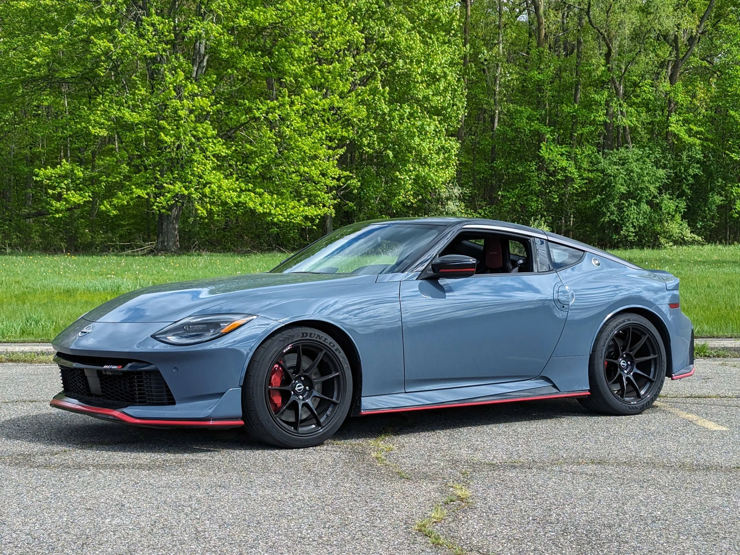 A sleek blue sports car parked on a paved surface with lush green trees in the background.
