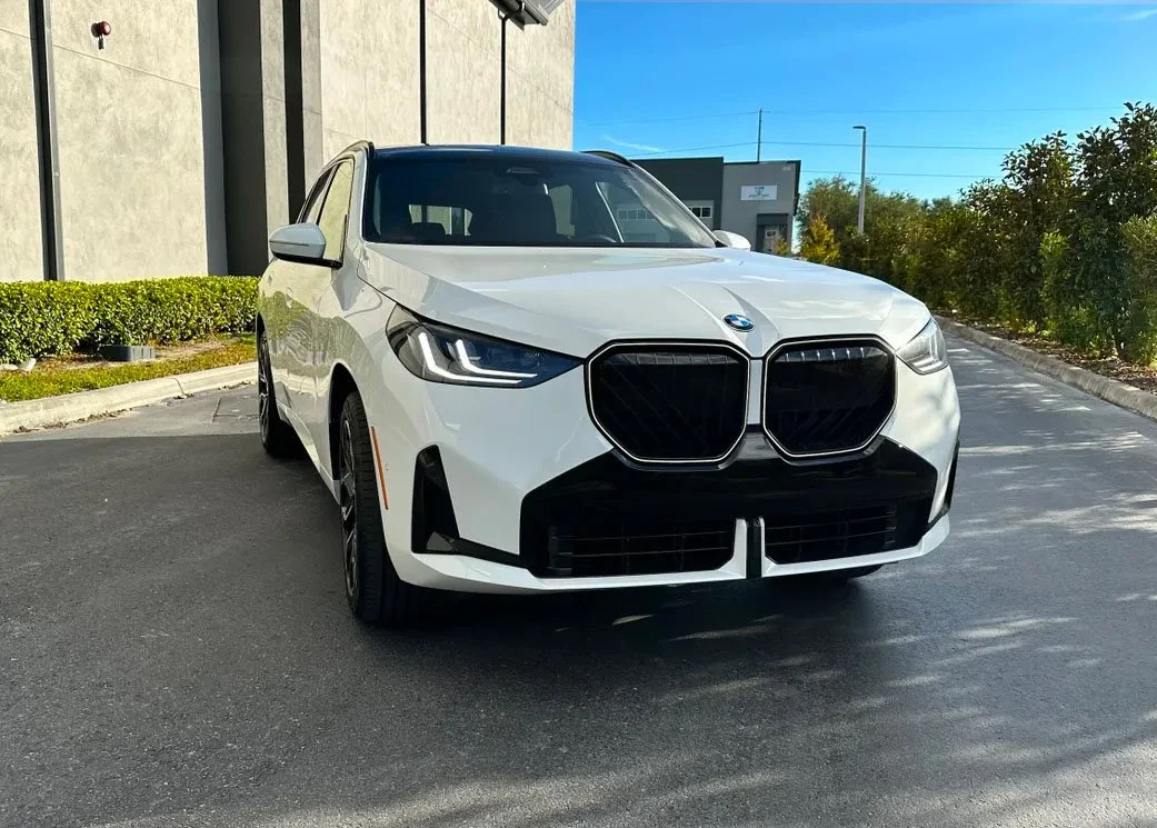 White BMW SUV parked outdoors with modern building in background.