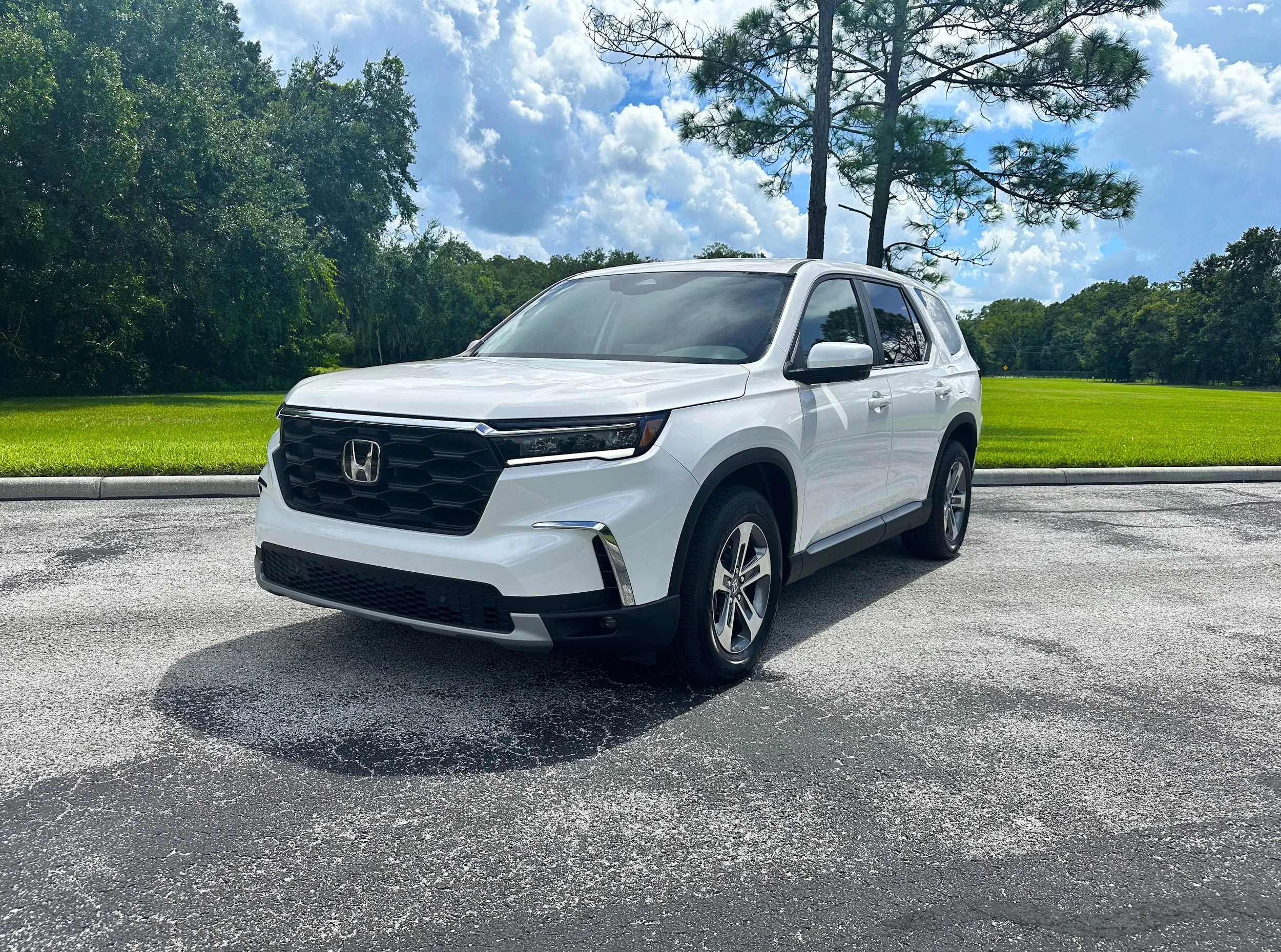 White Honda SUV parked on a paved road with green grass and trees in the background.