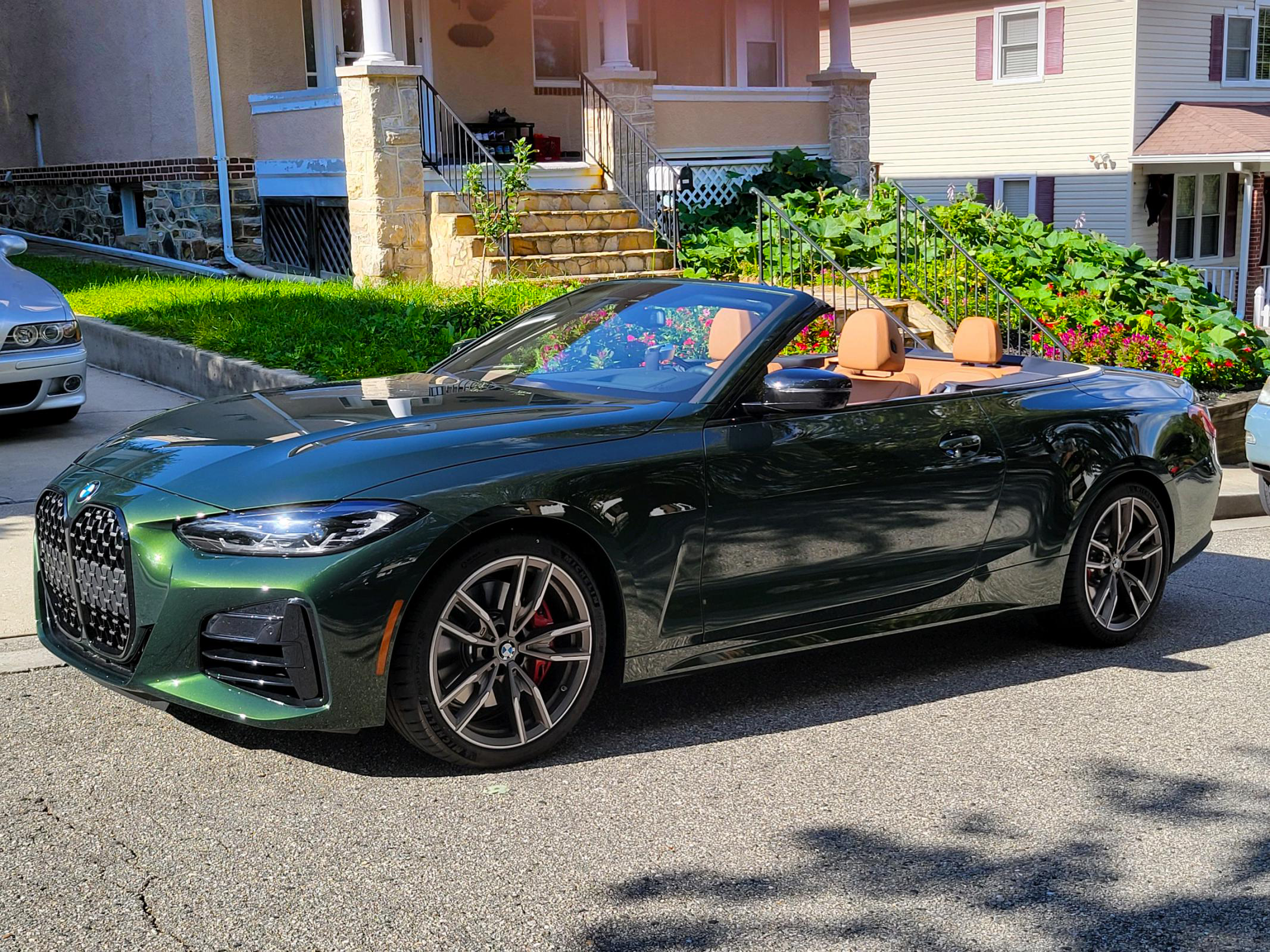 Green convertible car parked on a residential street with houses and greenery in the background.