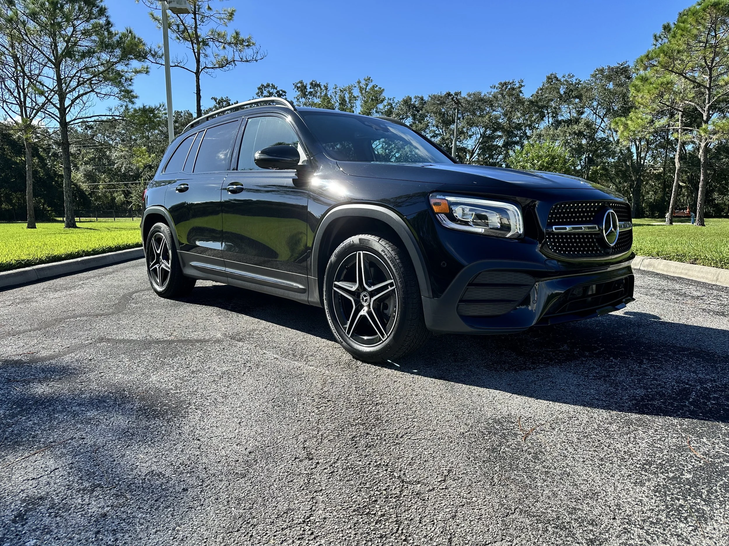 Black Mercedes-Benz SUV parked on a paved road with trees and grass in the background under a clear blue sky.