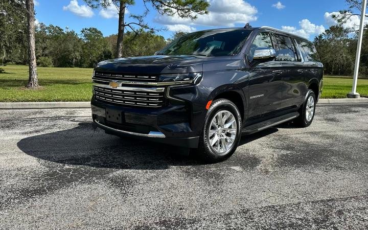 A black Chevrolet SUV parked on a paved surface with trees and grass in the background on a sunny day.