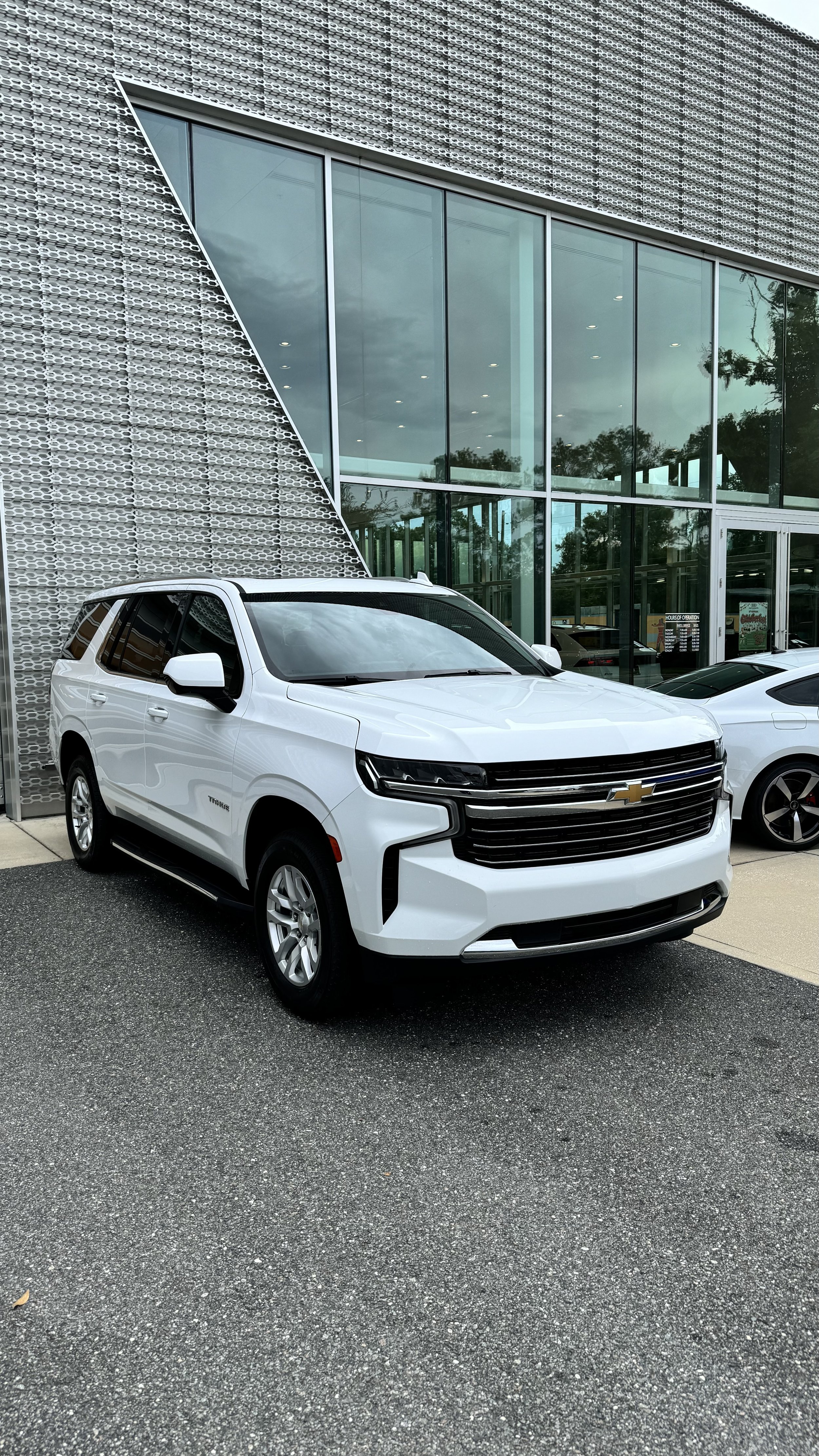 White Chevrolet SUV parked in front of a modern building with large glass windows.