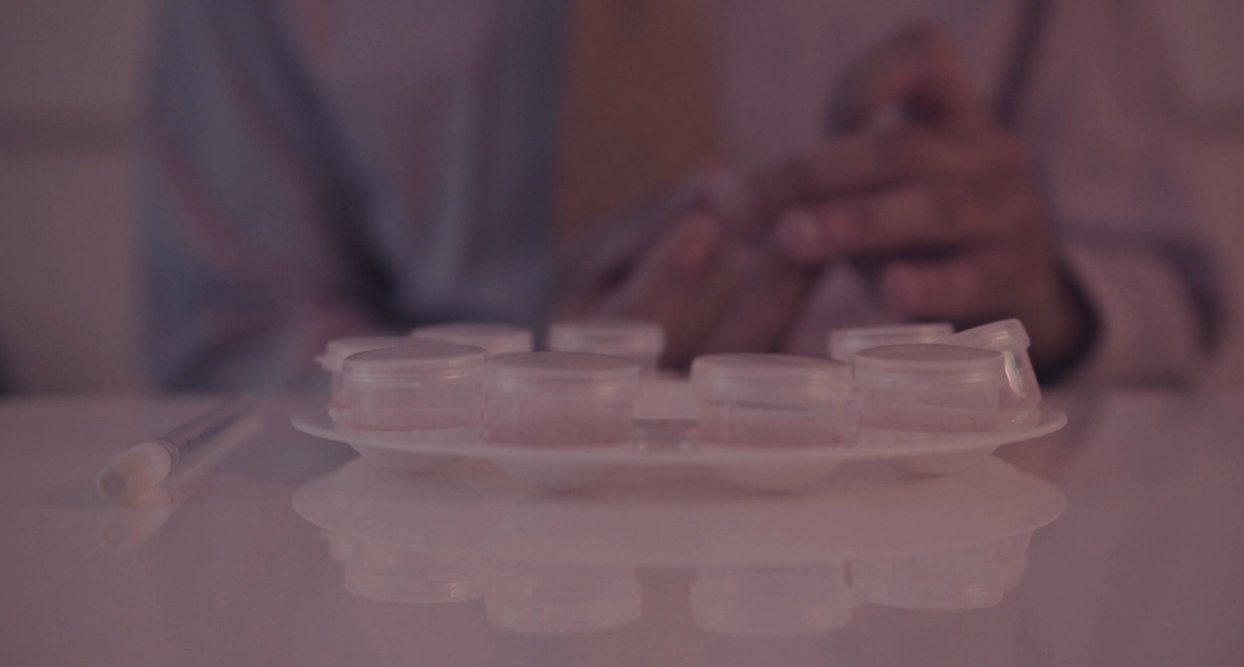 A person with clasped hands sitting at a table with a pack of clear plastic circular containers and a white pen.