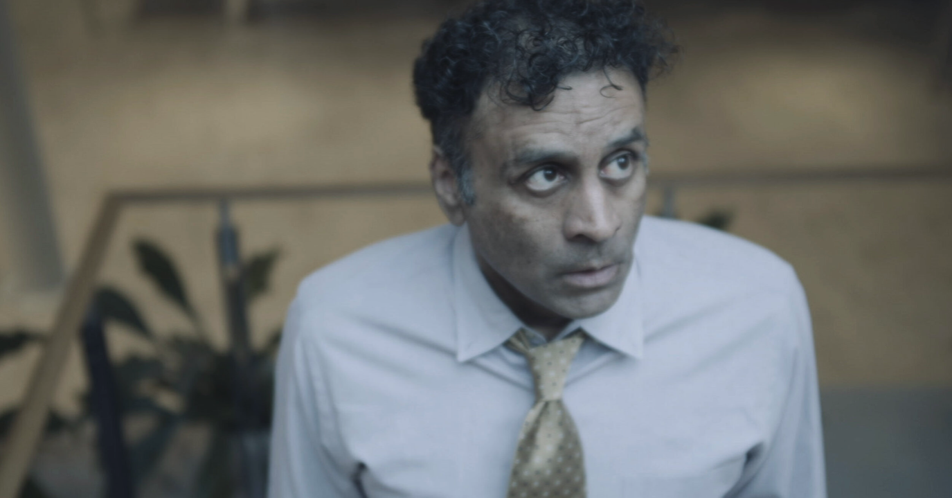 A man with disheveled hair and dirt on his face, wearing a white shirt and a tan polka dot tie, looking upward with a surprised or concerned expression.