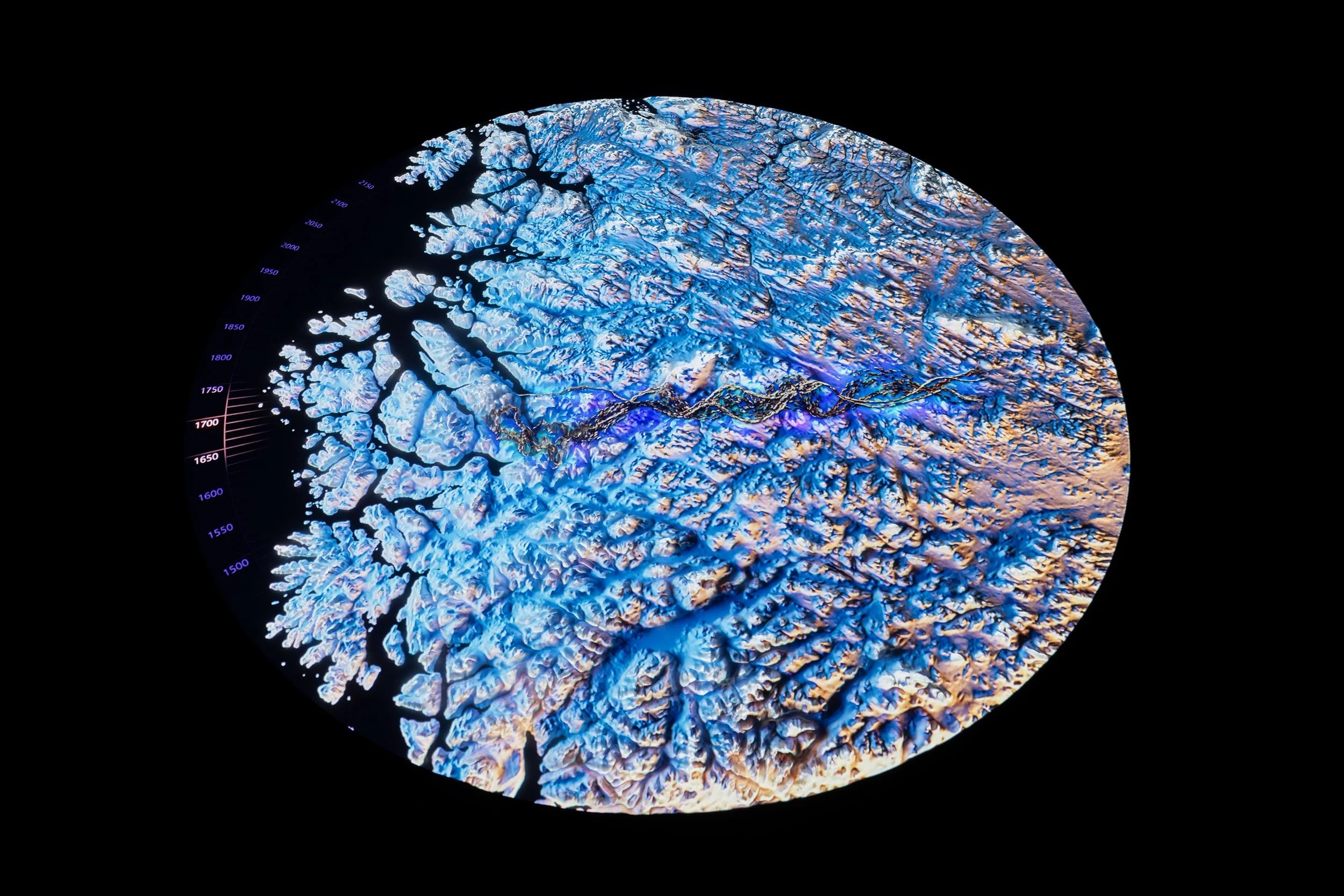Satellite view of a coastal icy landscape with icebergs and fjords, showing blue and white ice formations and dark channels.