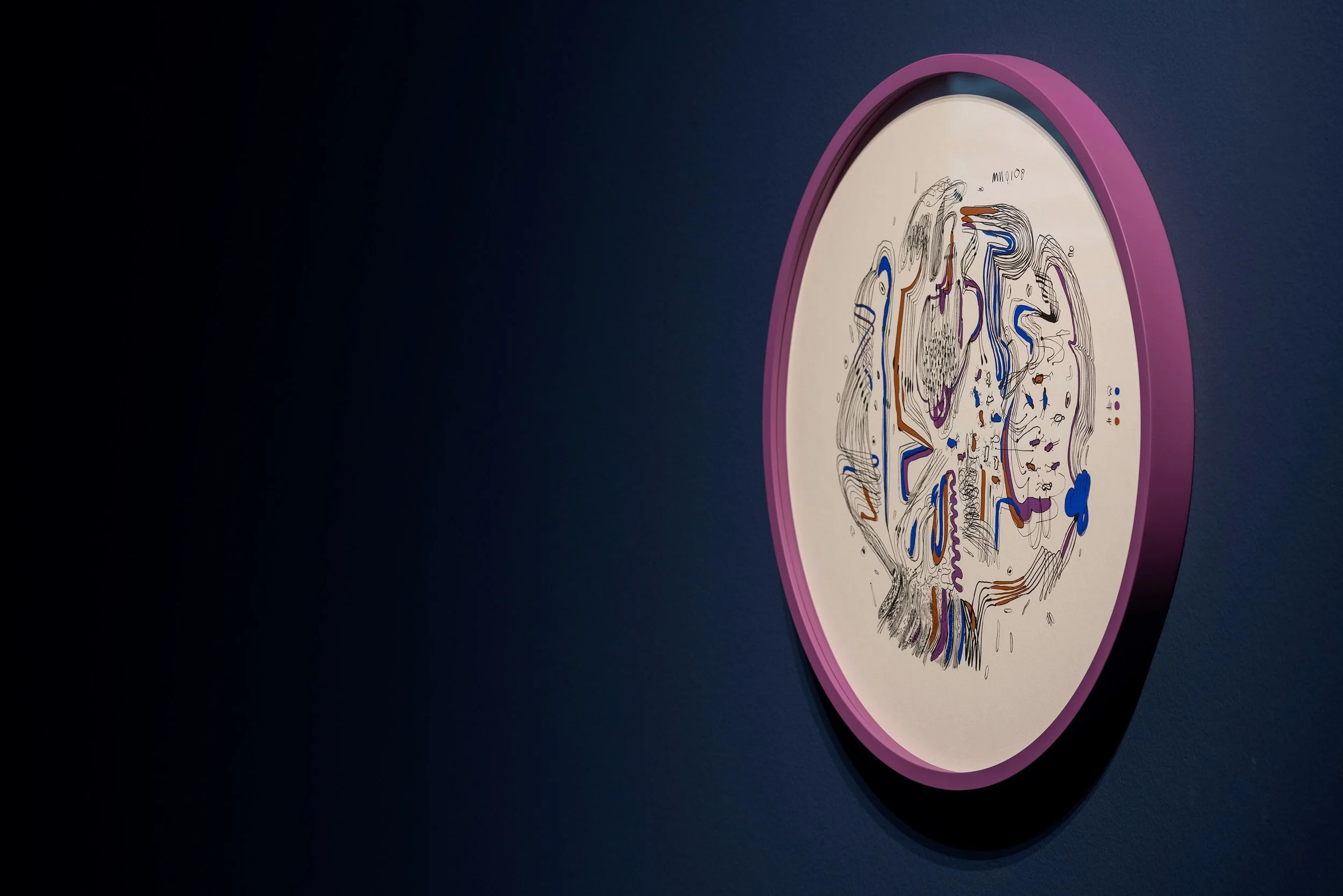 A colorful abstract art piece inside a pink oval frame against a dark blue wall.