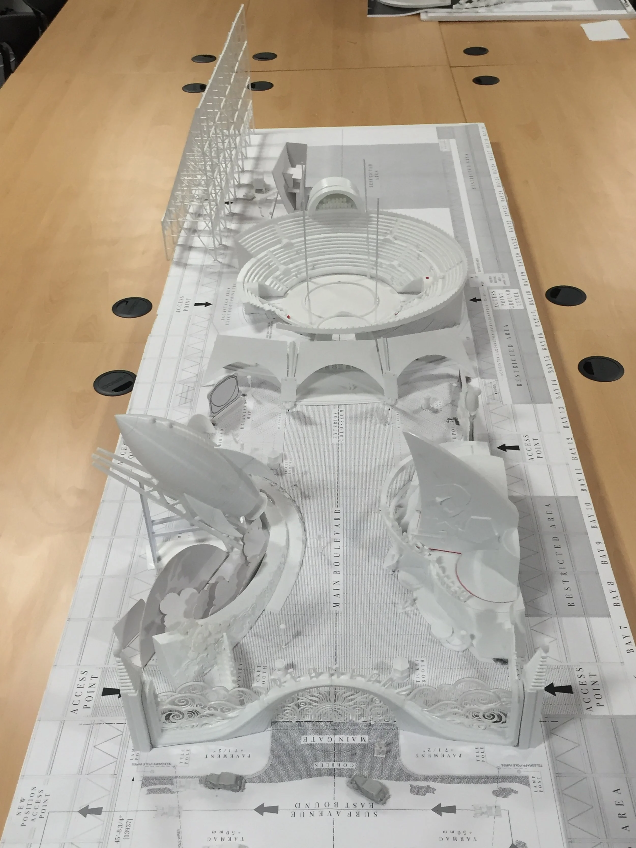 A white architectural model of a large building with multiple sections, open seating area, and intricate design details on the base, placed on a large table.