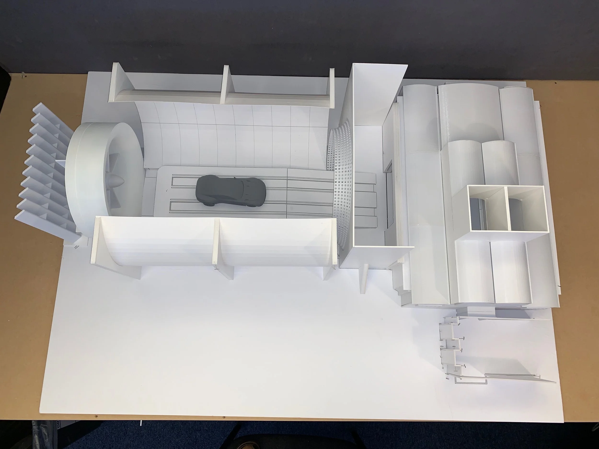 White architectural model of a modern building or interior space with open shelves, a central circular feature, and a model car on a flat surface.