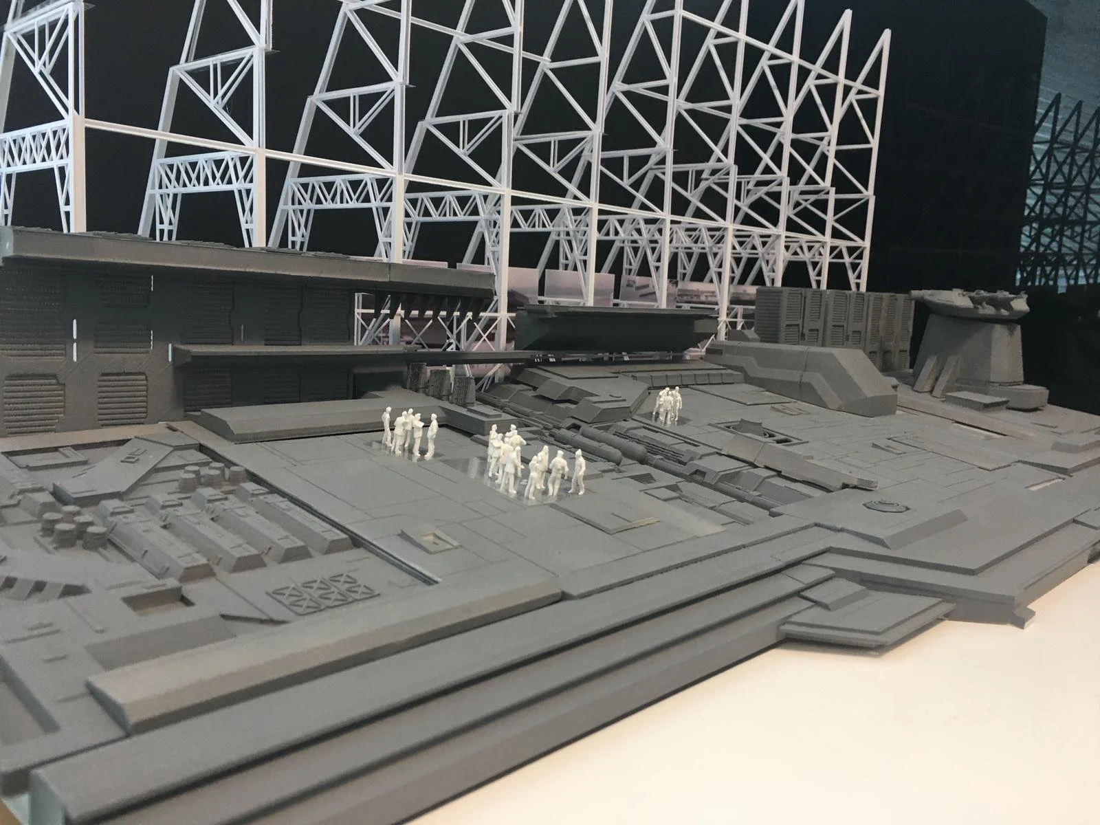 A detailed scale model of a futuristic spaceship or space station with miniature figures of people on it, set against a backdrop of a complex lattice structure.