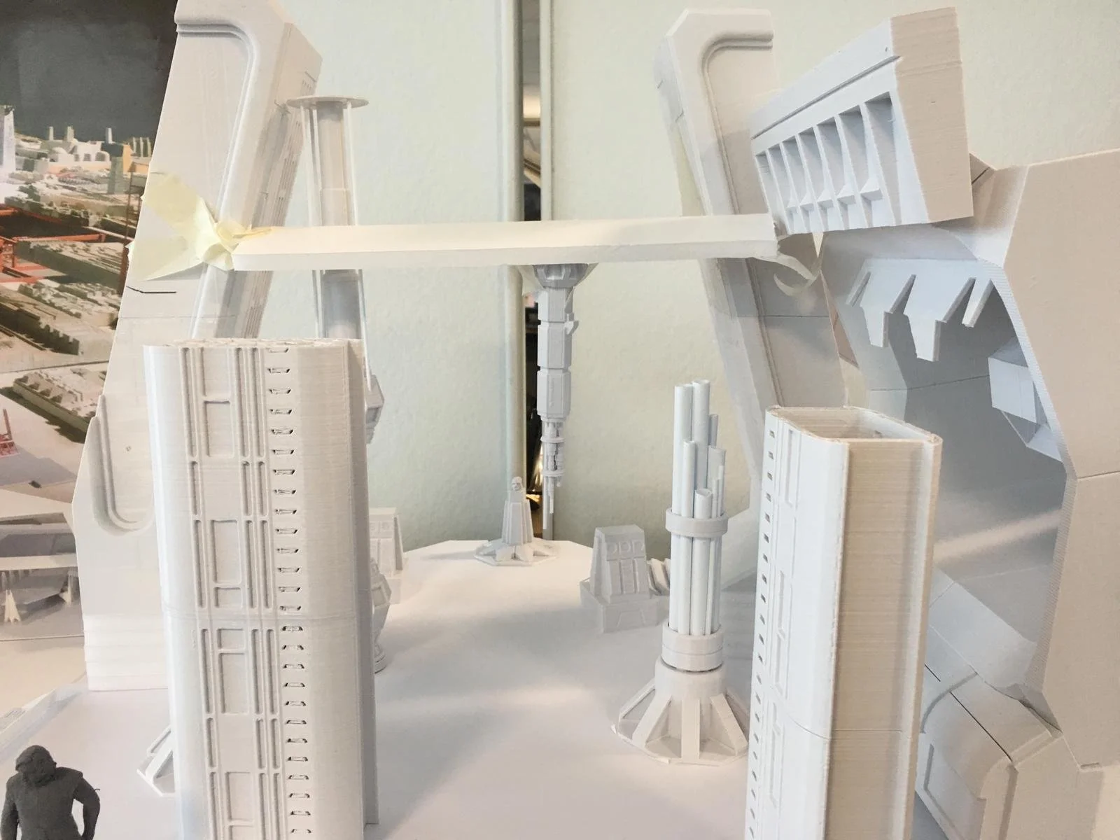 A white architectural model of a cityscape with various high-rise buildings, towers, and structures made of foam or plastic, placed on a white surface.