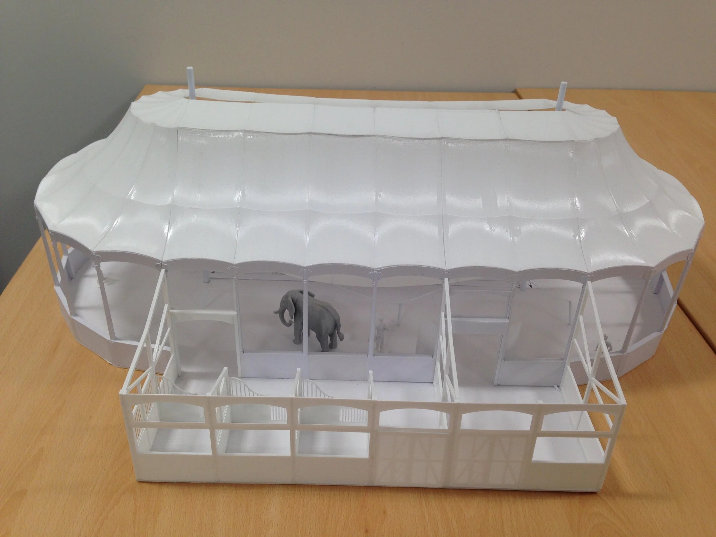 White architectural model of a building with a large curved roof, open sides, and a small elephant figurine inside.
