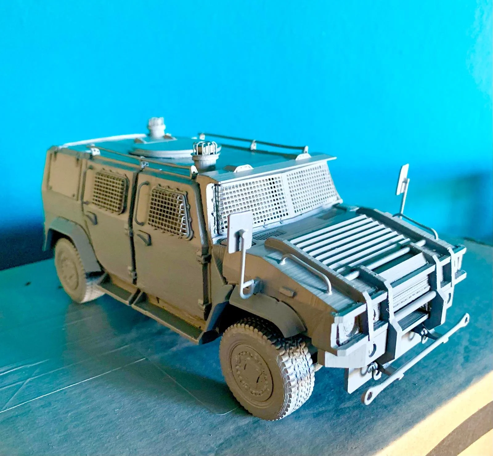 Model of a military Humvee vehicle made out of wood with detailed features like a grill, wheels, and antenna, set against a light blue background.