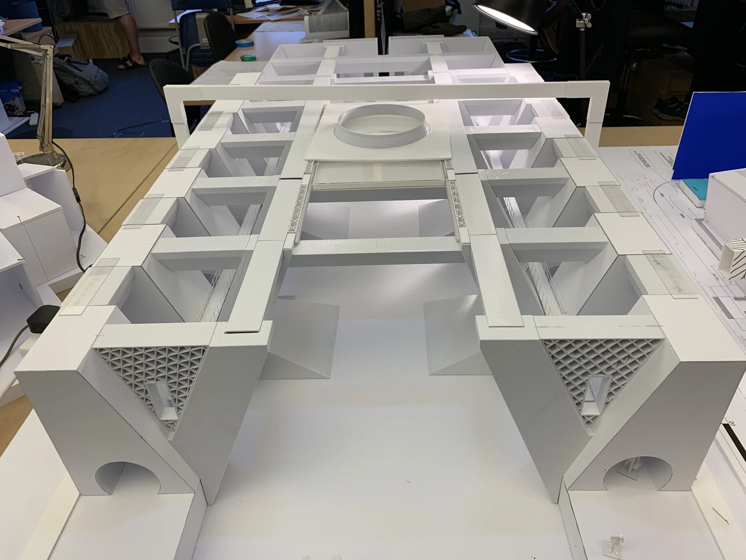 Scale model of a building with a grid-like structure, white exterior, and various geometric openings, placed on a table in an indoor setting.