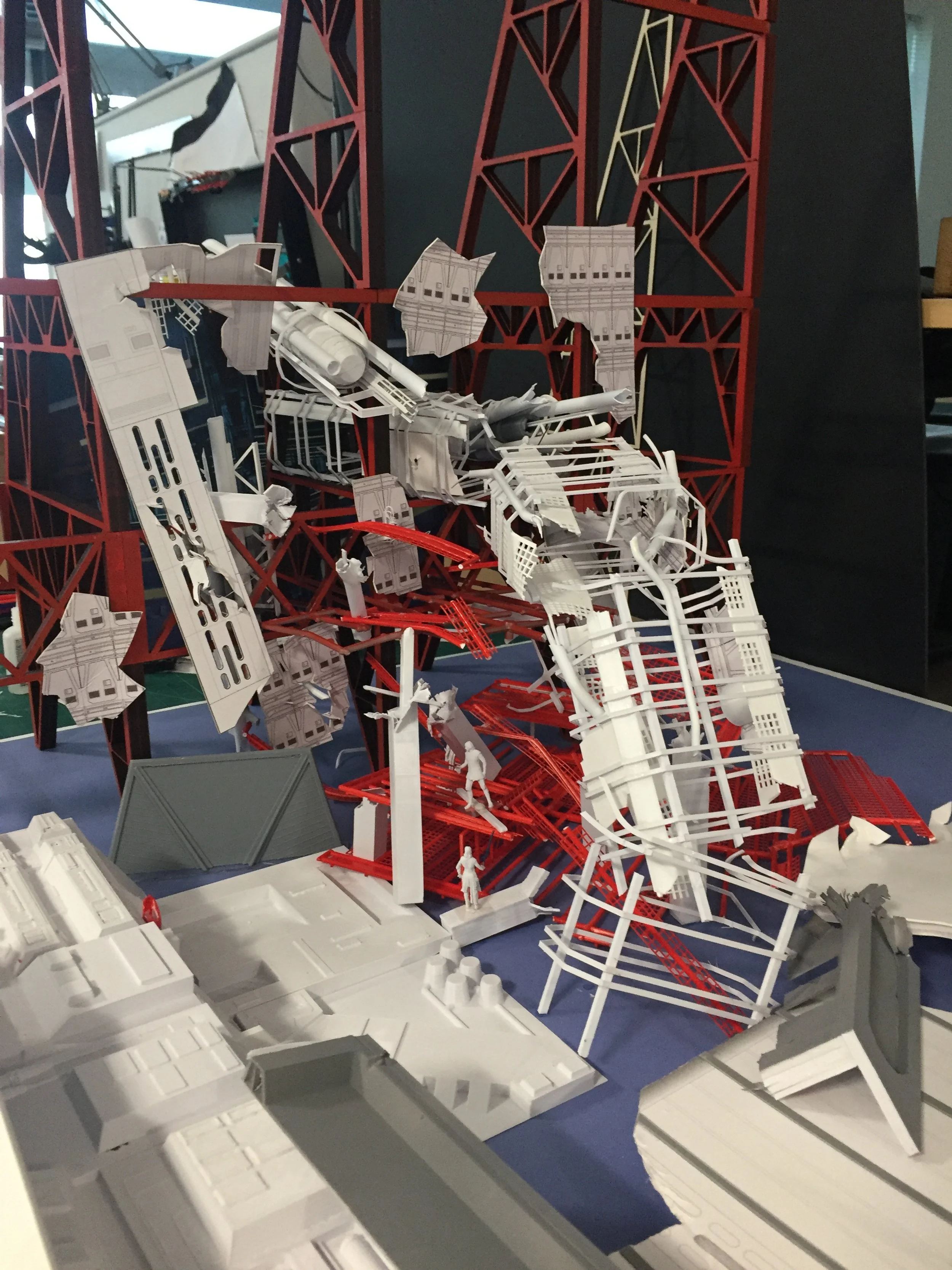 Detailed architectural model of a crashed building or structure with red and white frameworks, miniature human figures, and surrounding base elements.