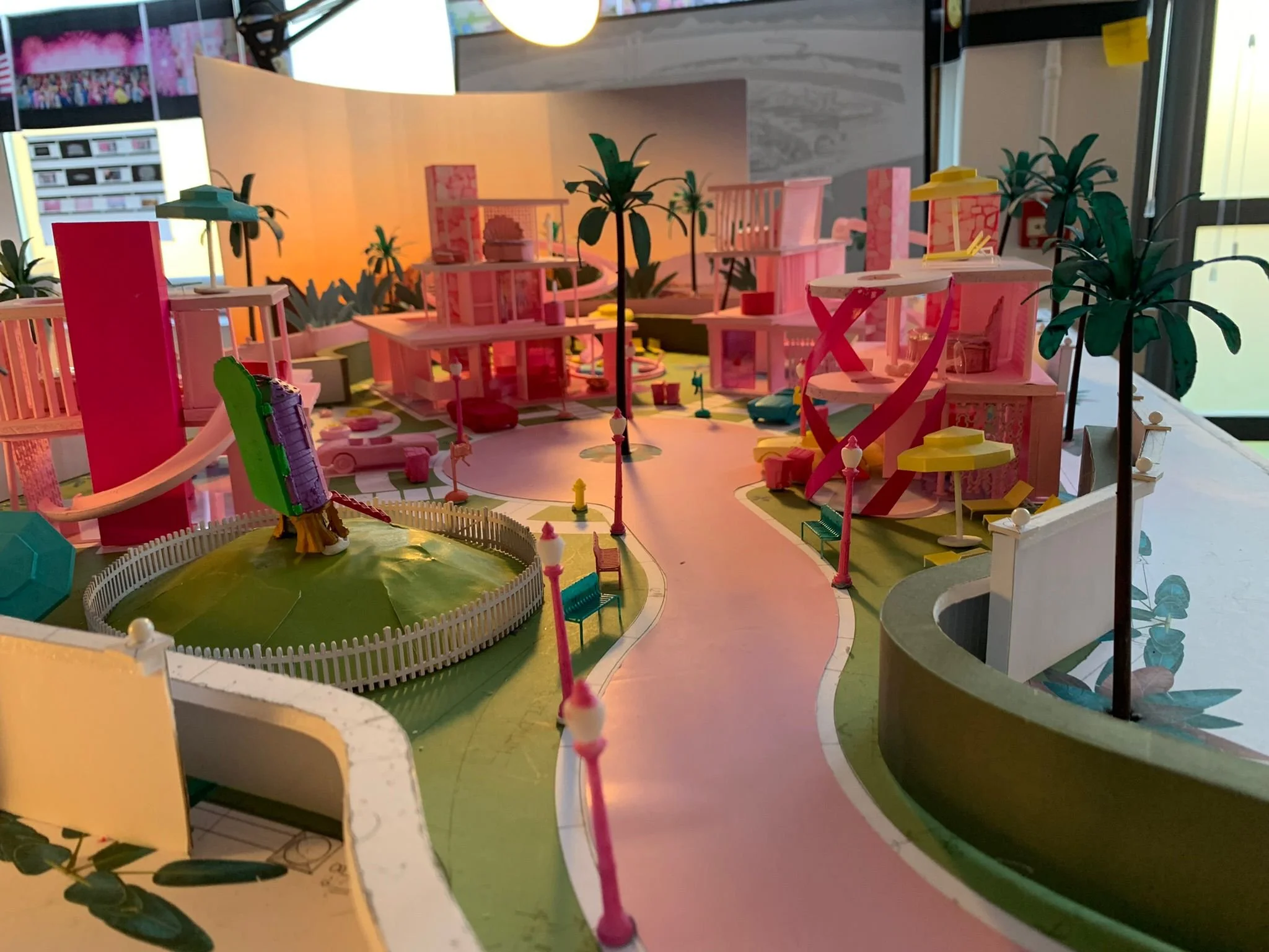 Colorful miniature model of a modern cityscape with pink buildings, street lamps, palm trees, and a winding road.