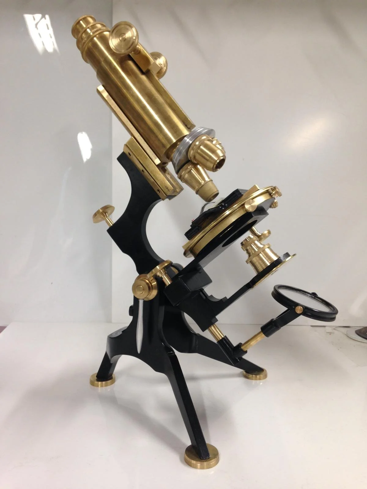 A vintage brass microscope with black accents on a white surface against a plain white background.
