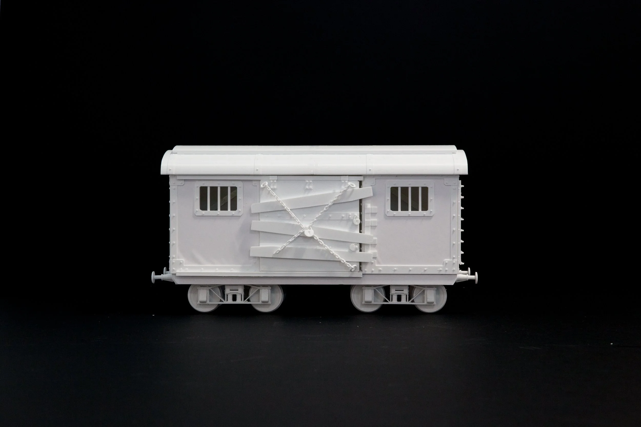 A white model train boxcar with barred windows and a closed door, set against a black background.