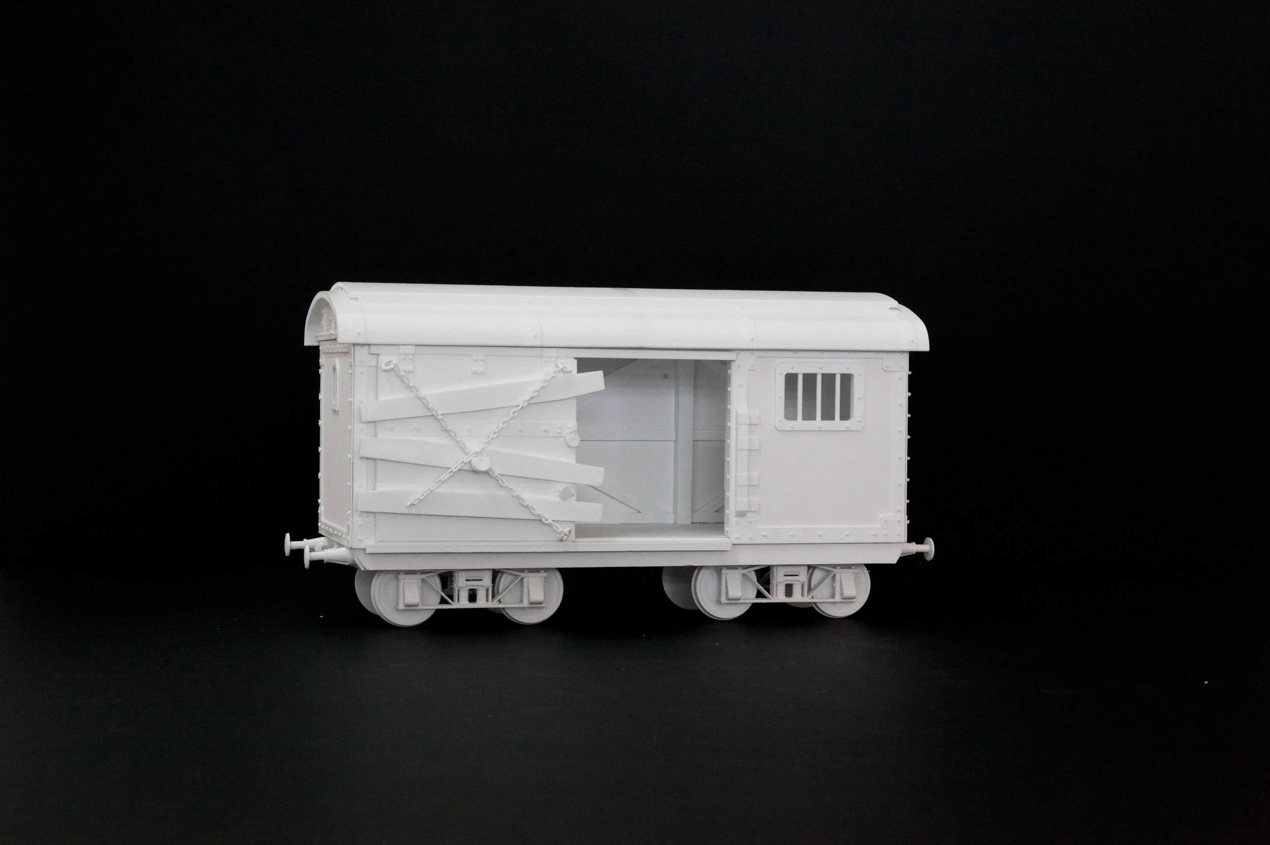 Unpainted miniature model train car against a black background.