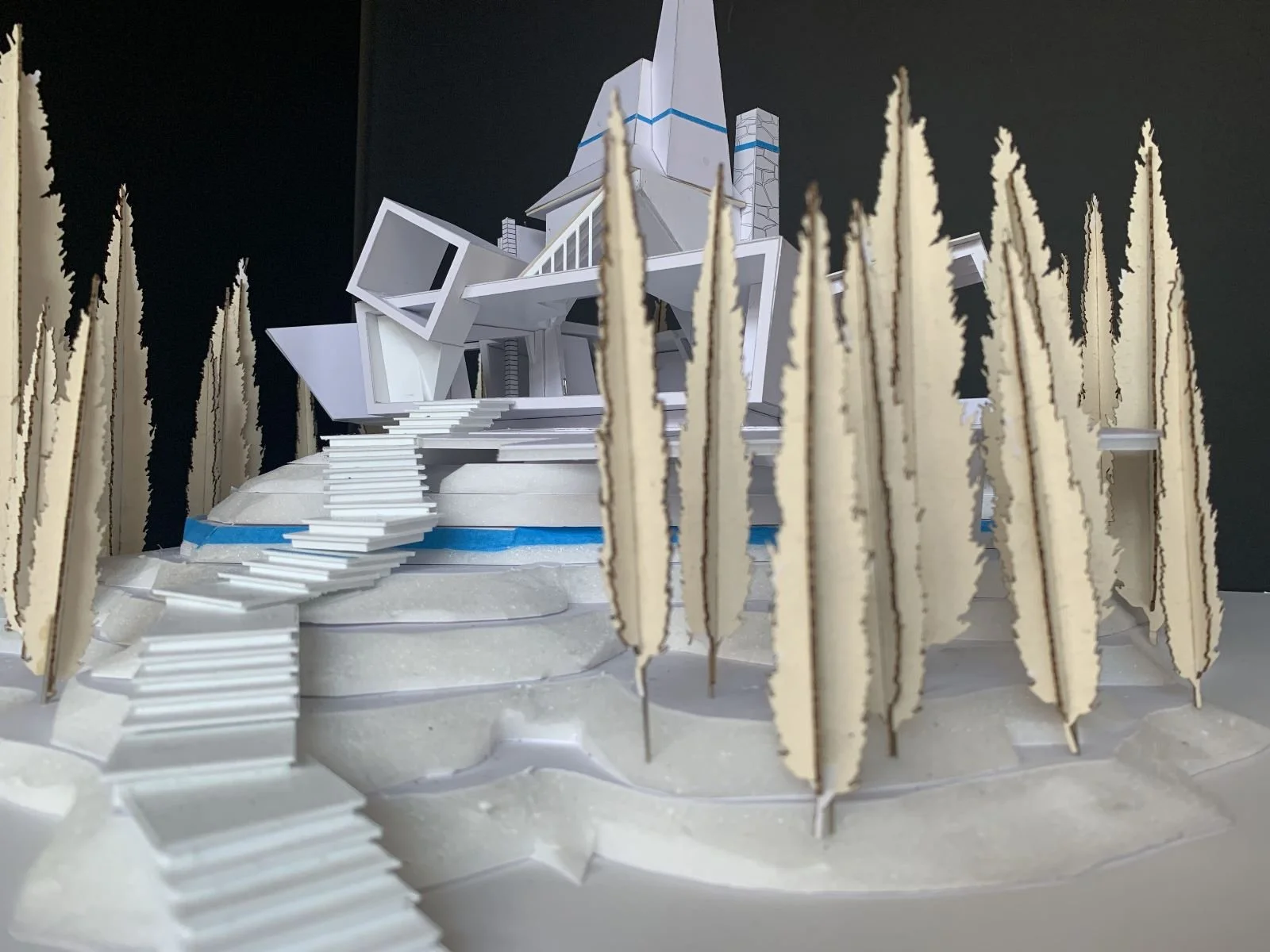 Architectural model of a modern house on a tiered, landscaped base, surrounded by tall, cut-out trees.