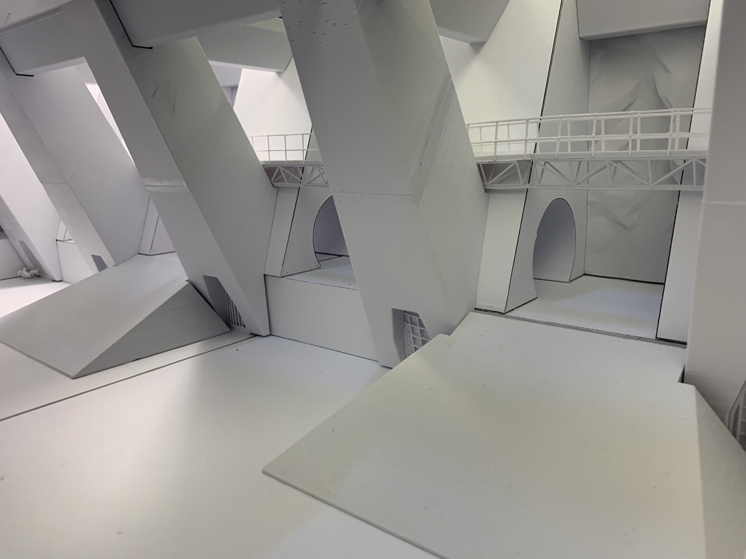 A white architectural model featuring multiple large, angular structures with archways, walkways, and balconies.