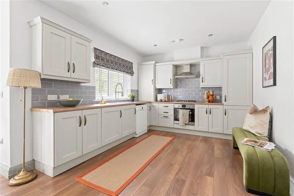Kitchen with white cabinets, gray subway tile backsplash, wooden countertops, window with blinds, green bench with pillows, and wooden floor.
